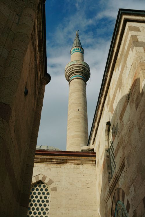 Free View of a tall minaret rising against a clear blue sky between historical stone buildings. Stock Photo