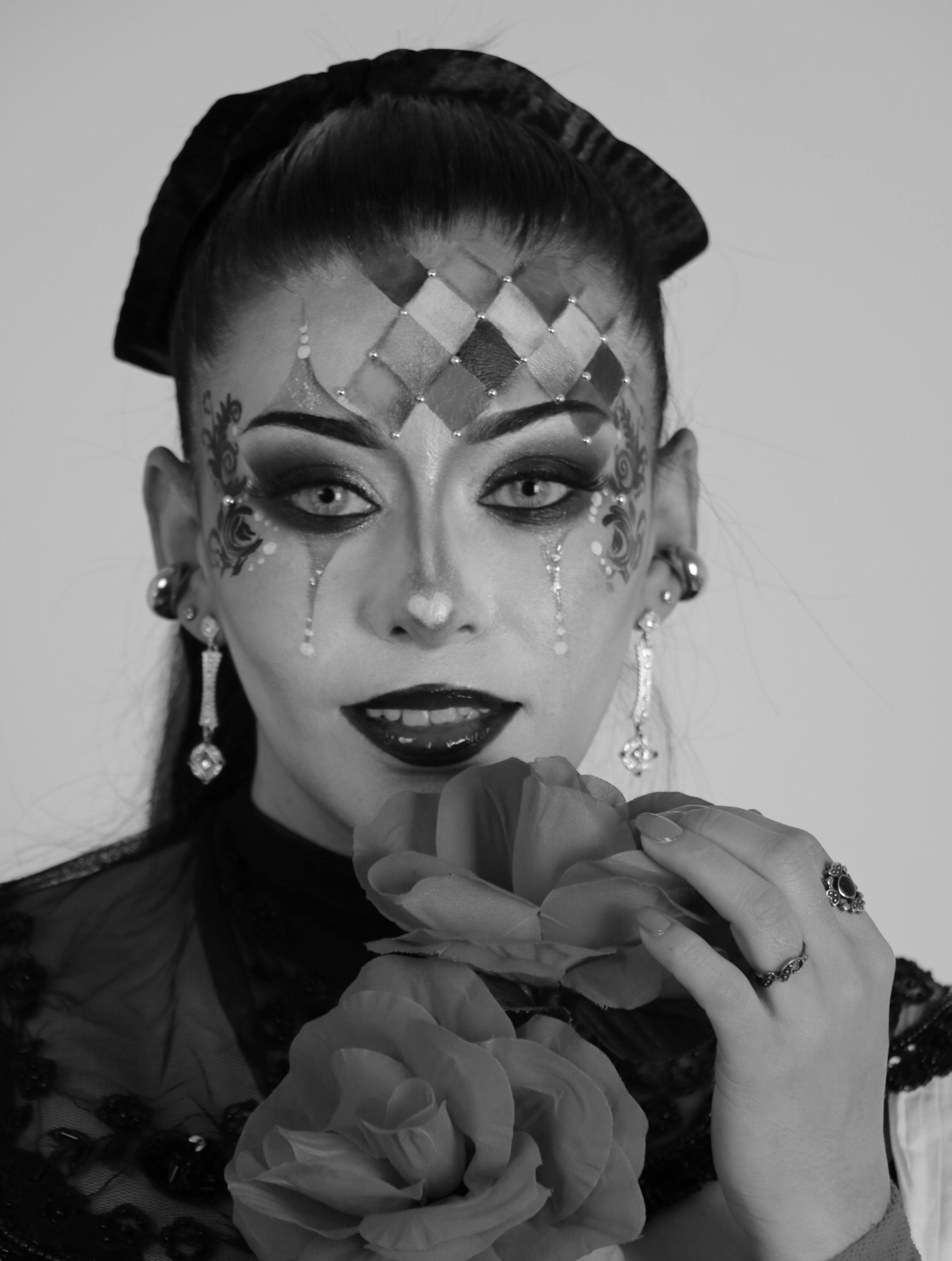 Gratis Gambar close-up seorang wanita dengan riasan badut memegang mawar, menampilkan seni dan keanggunan yang dramatis. Foto Stok