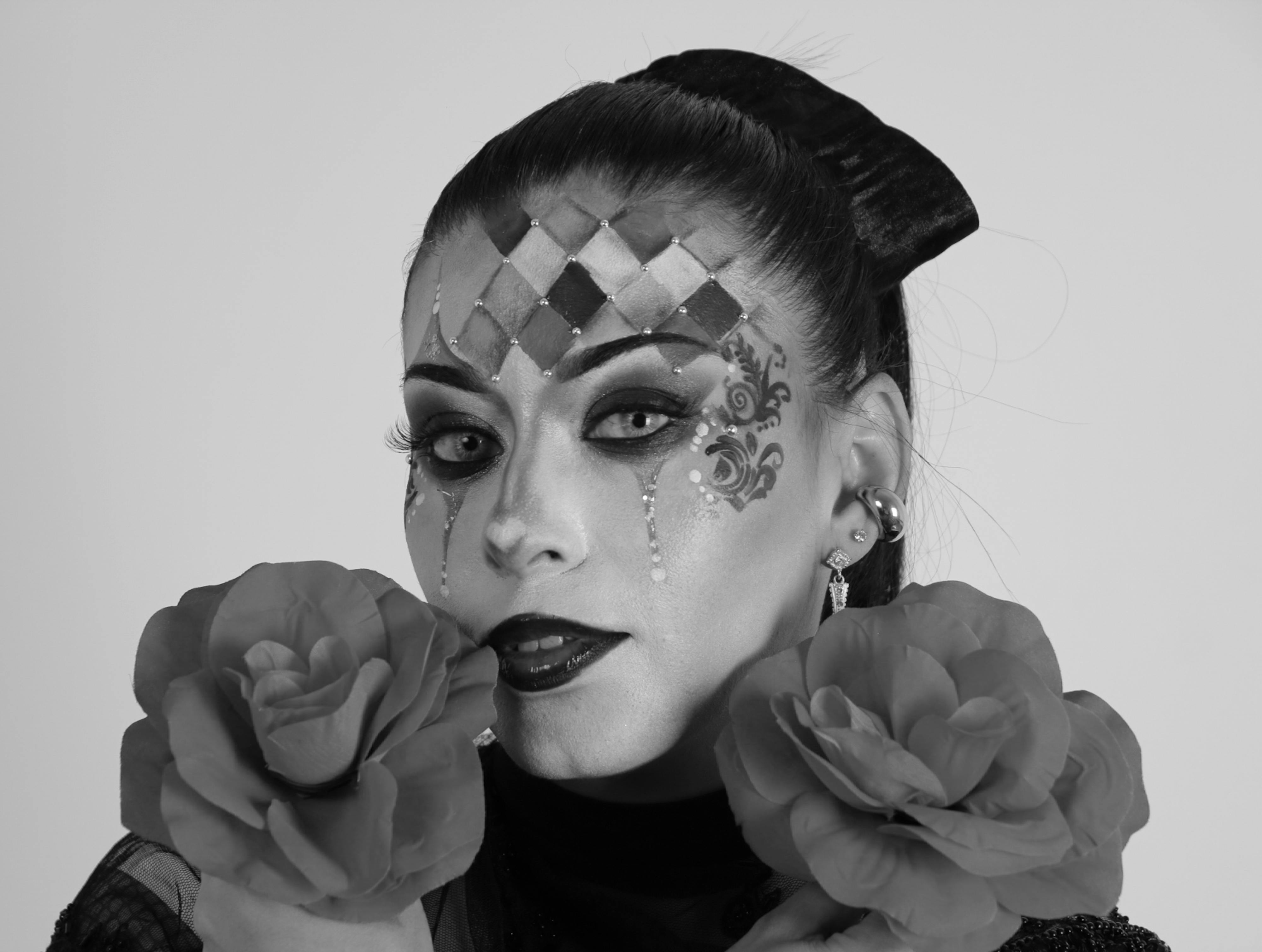Bezpłatne Dramatyczny czarno-biały portret z misternym makijażem twarzy i różami, wywołujący tajemniczy i artystyczny nastrój. Zdjęcie z galerii