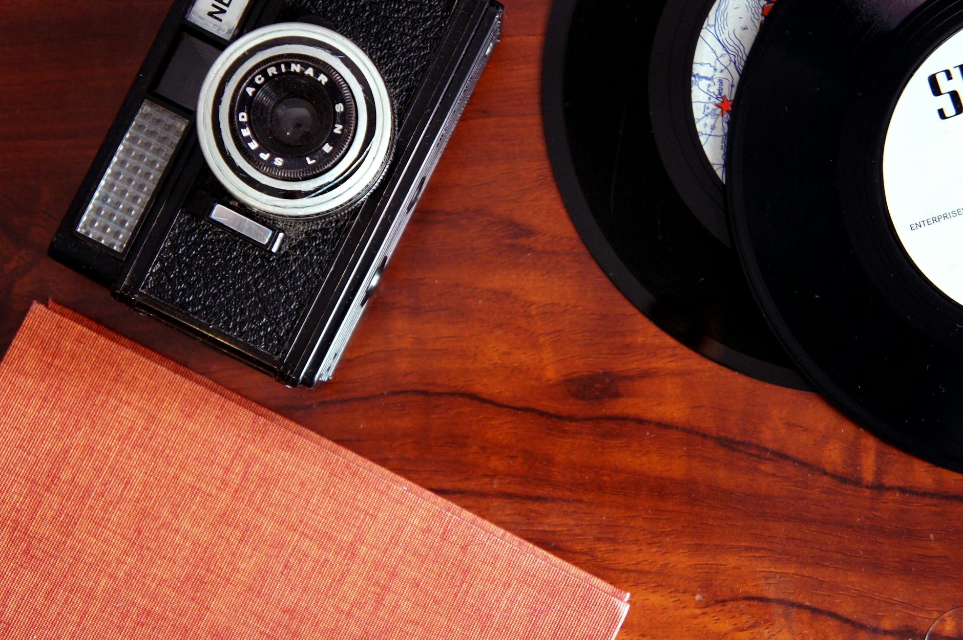 An artistic display of a vintage camera and vinyl records on a polished wooden desk.
