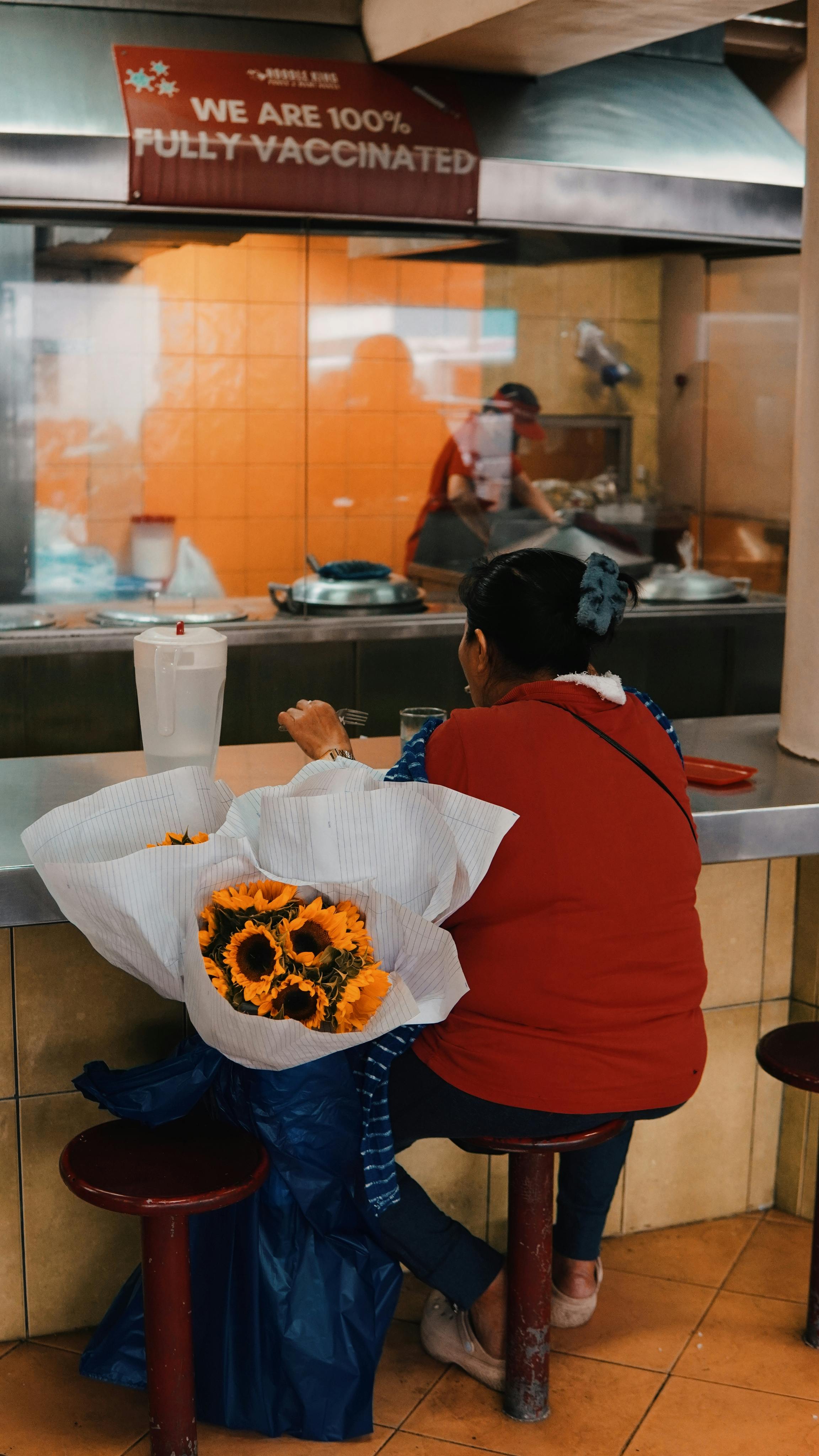 Bezpłatne Kobieta siedząca przy ladzie w restauracji, obok niej bukiet słoneczników. Zdjęcie z galerii