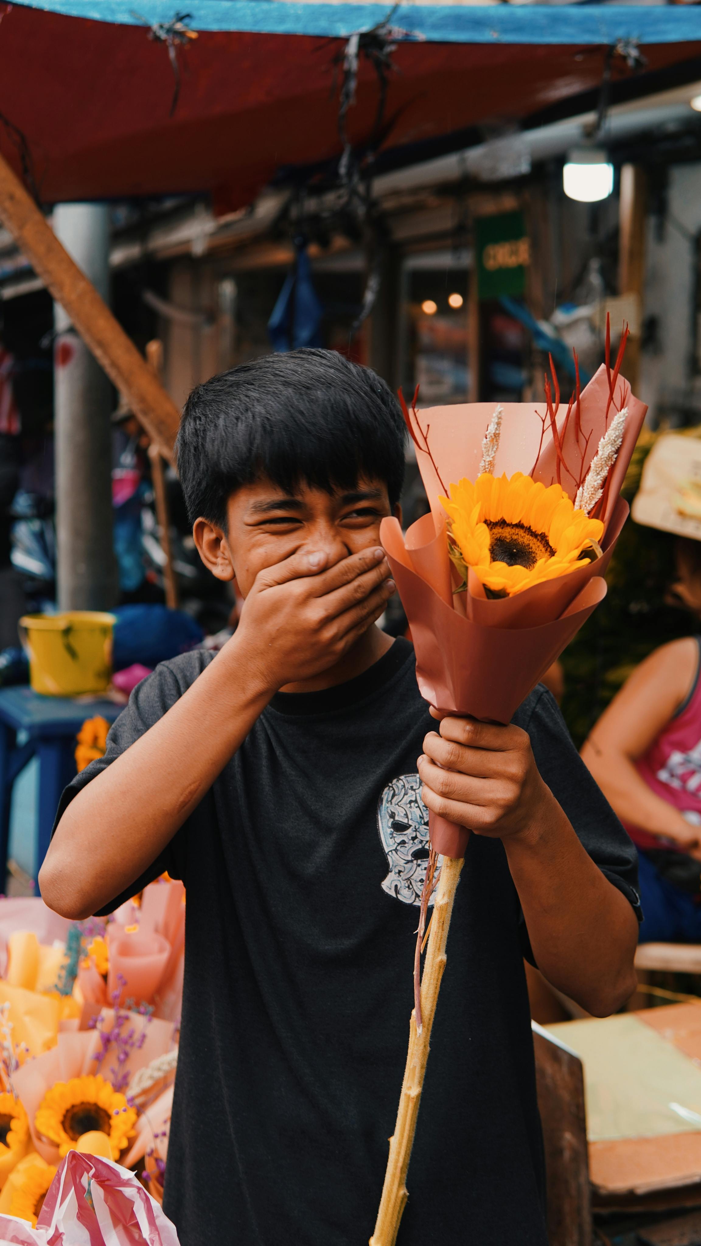 Bezpłatne Śmiejący się nastolatek trzyma bukiet słoneczników na targu pod gołym niebem. Zdjęcie z galerii
