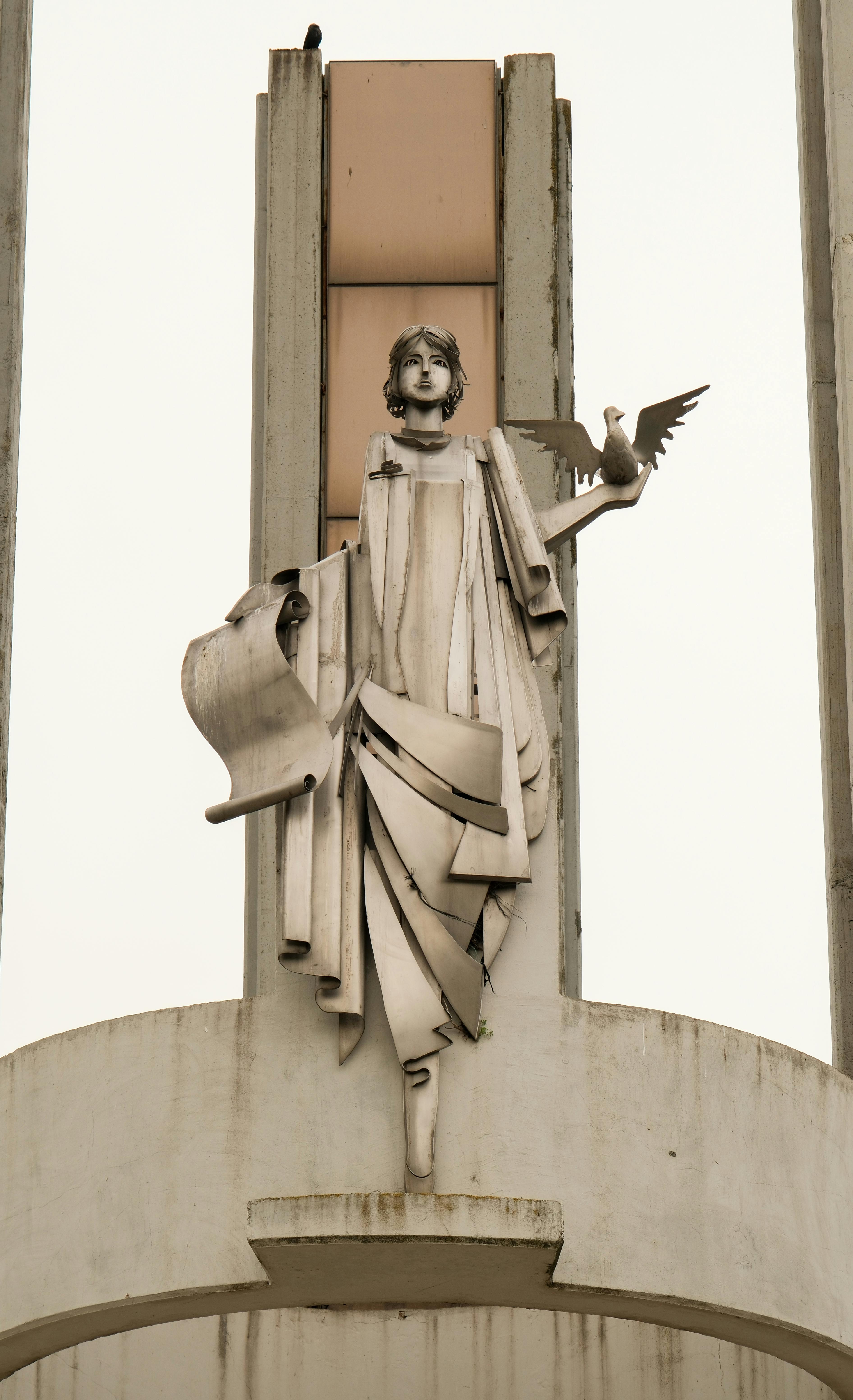 Gratis En detaljeret skulptur af en engel, der holder en fugl oven på en historisk bygning, der fremviser arkitektonisk elegance. Lagerfoto