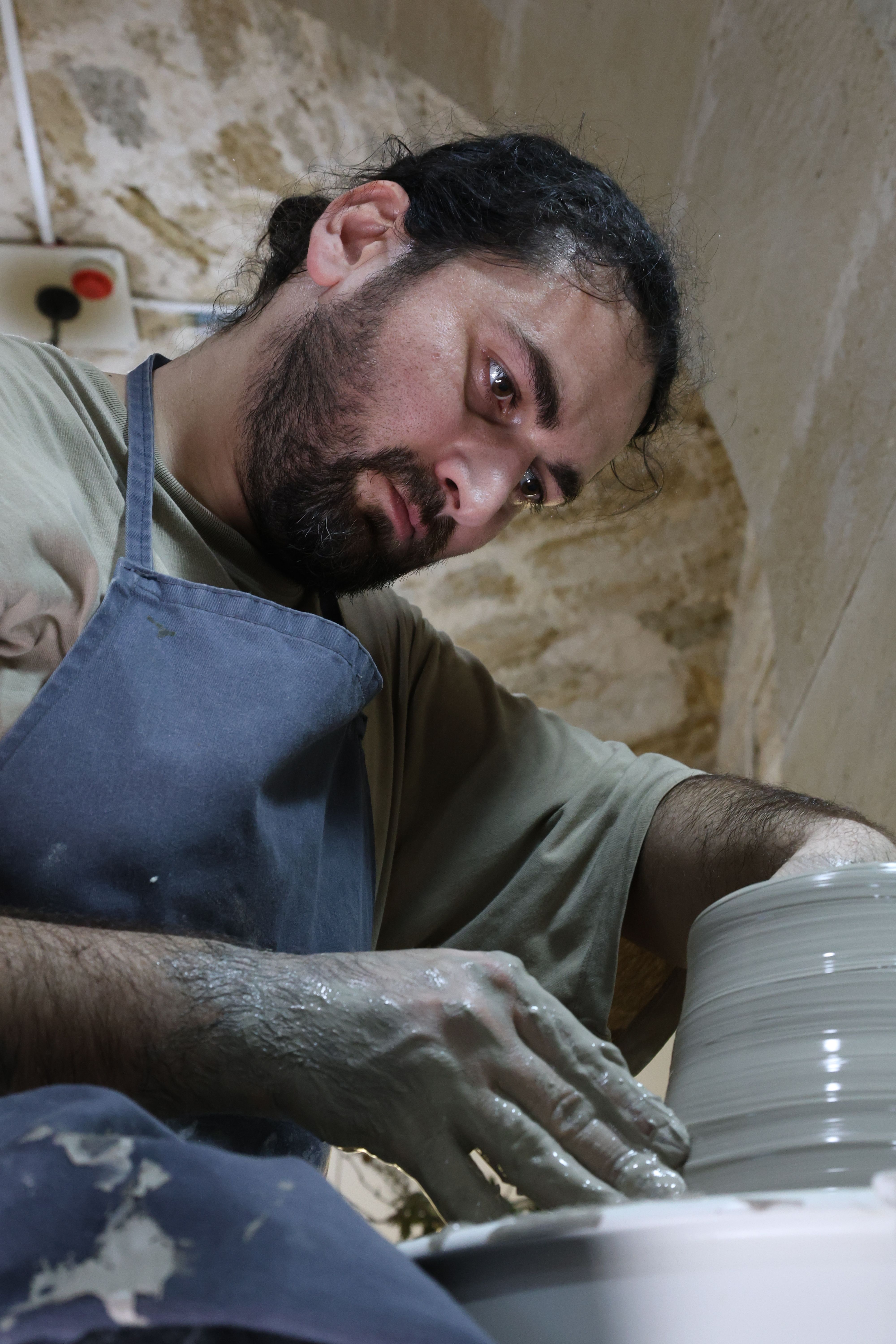 A focused artisan shaping clay on a pottery wheel in a traditional workshop.