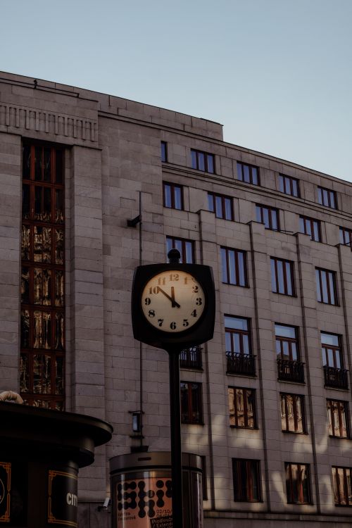 Free A street clock stands in front of a classic urban office building under clear skies. Stock Photo