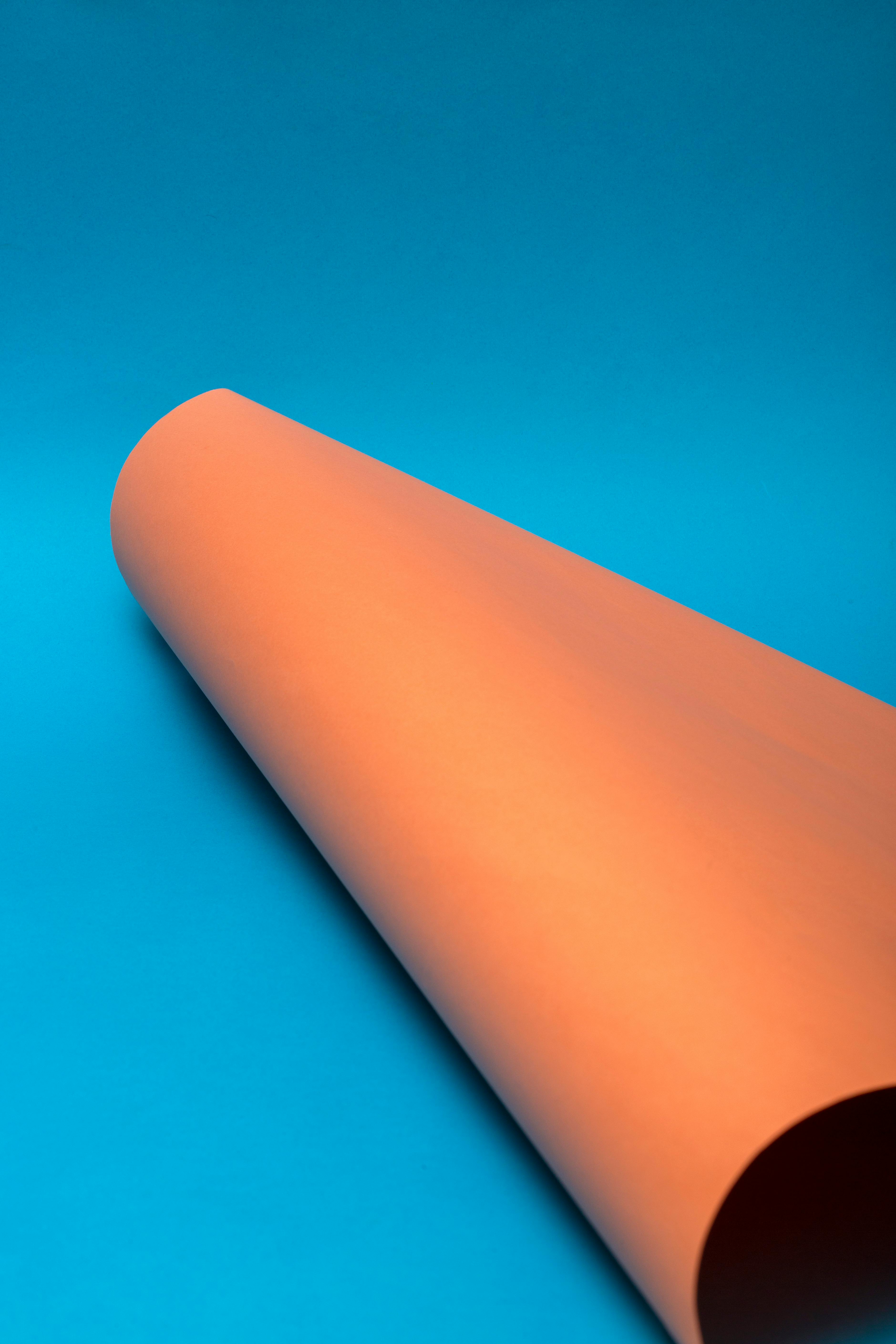 Free Orange paper roll on vivid blue background, perfect for modern design concepts. Stock Photo
