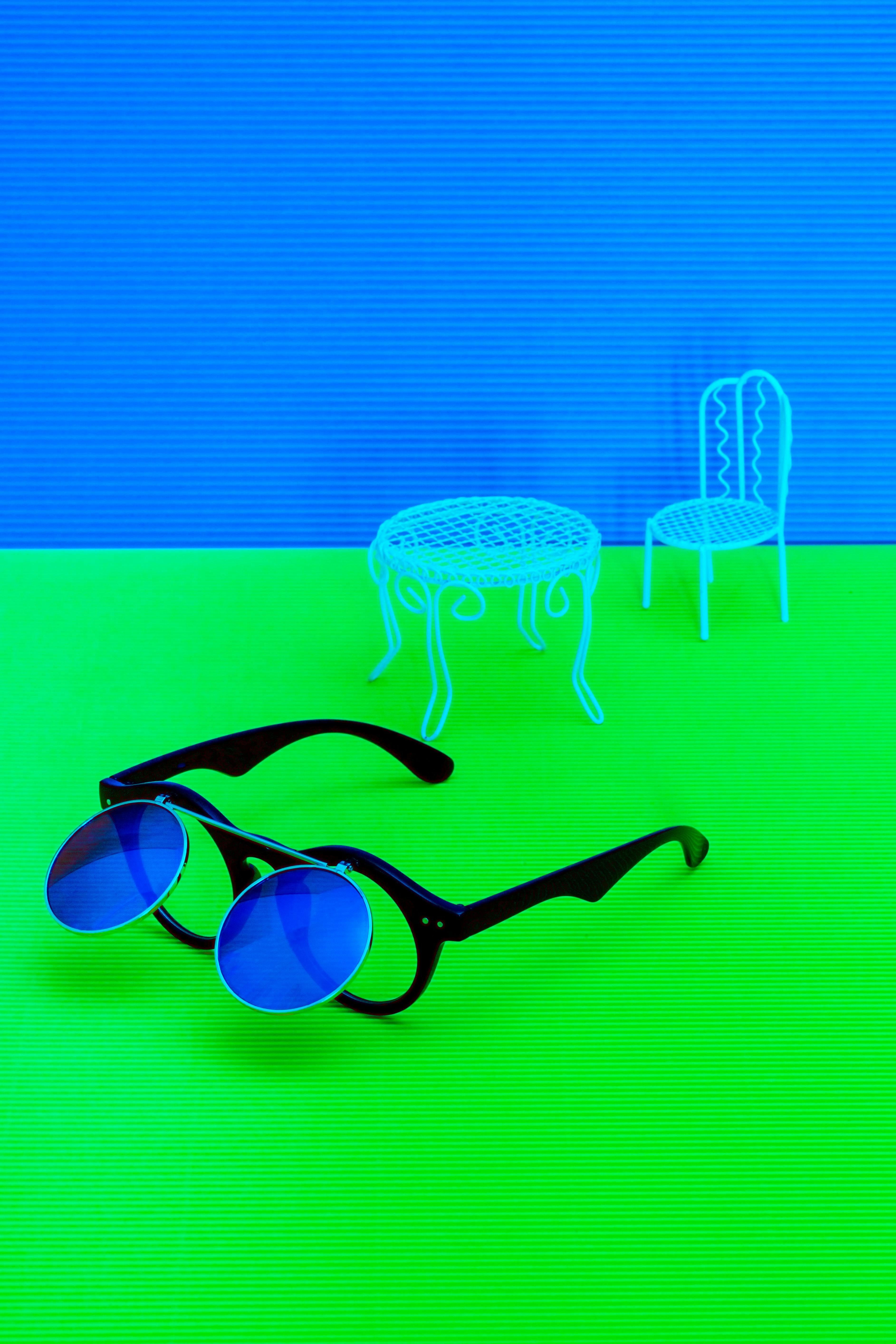 Free Vibrant scene with blue sunglasses, chairs, and table on a neon green background. Stock Photo