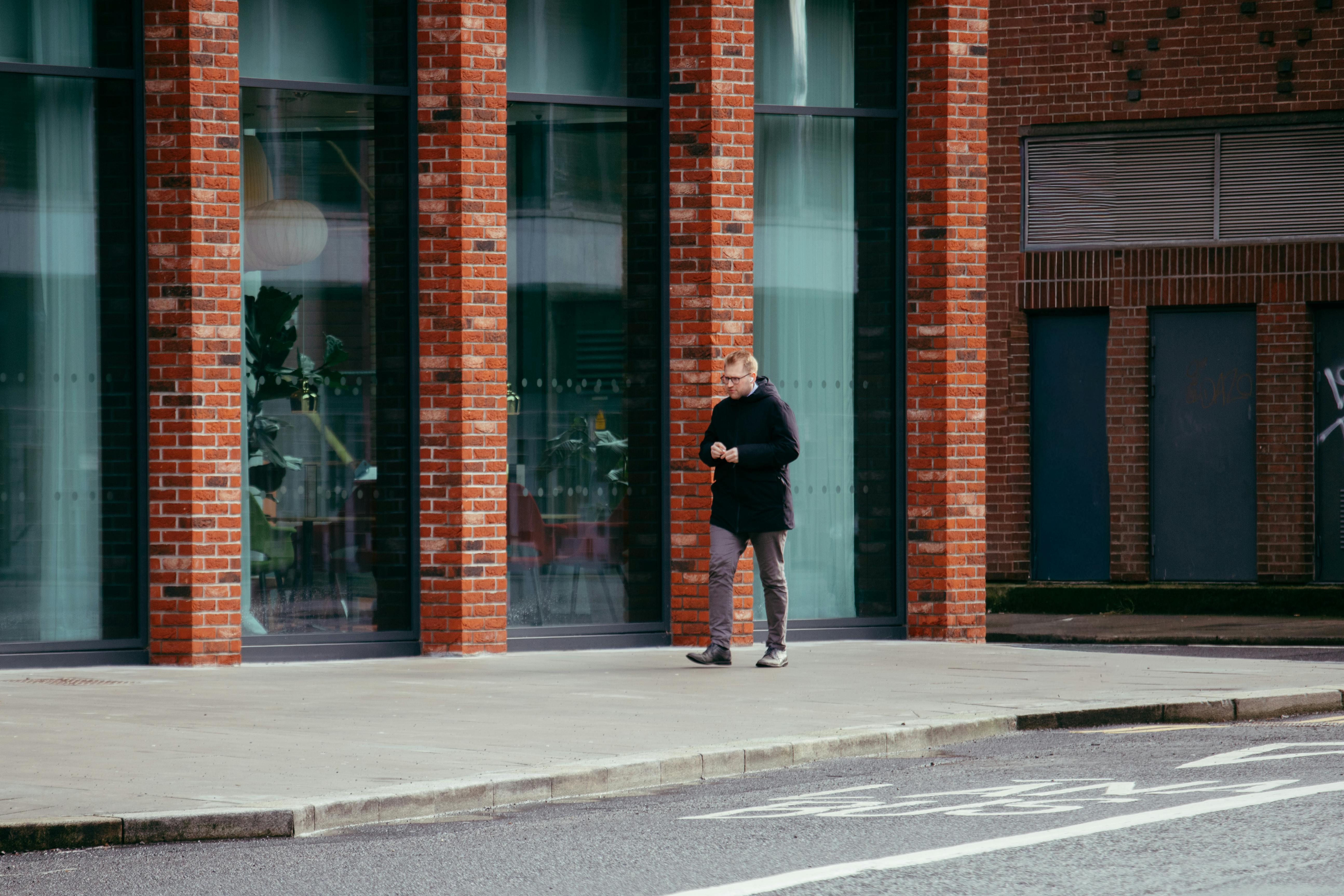 Gratuit Bărbat care merge cu un smartphone pe lângă o clădire modernă din cărămidă din comitatul Dublin, Irlanda. Fotografie de stoc
