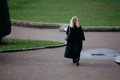 Free A woman in a black coat walks alone in a peaceful Dublin park on a rainy day. Stock Photo