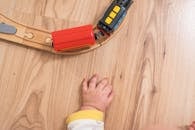 婴儿的手伸向镶木地板上的彩色木制玩具火车，促进玩耍和探索