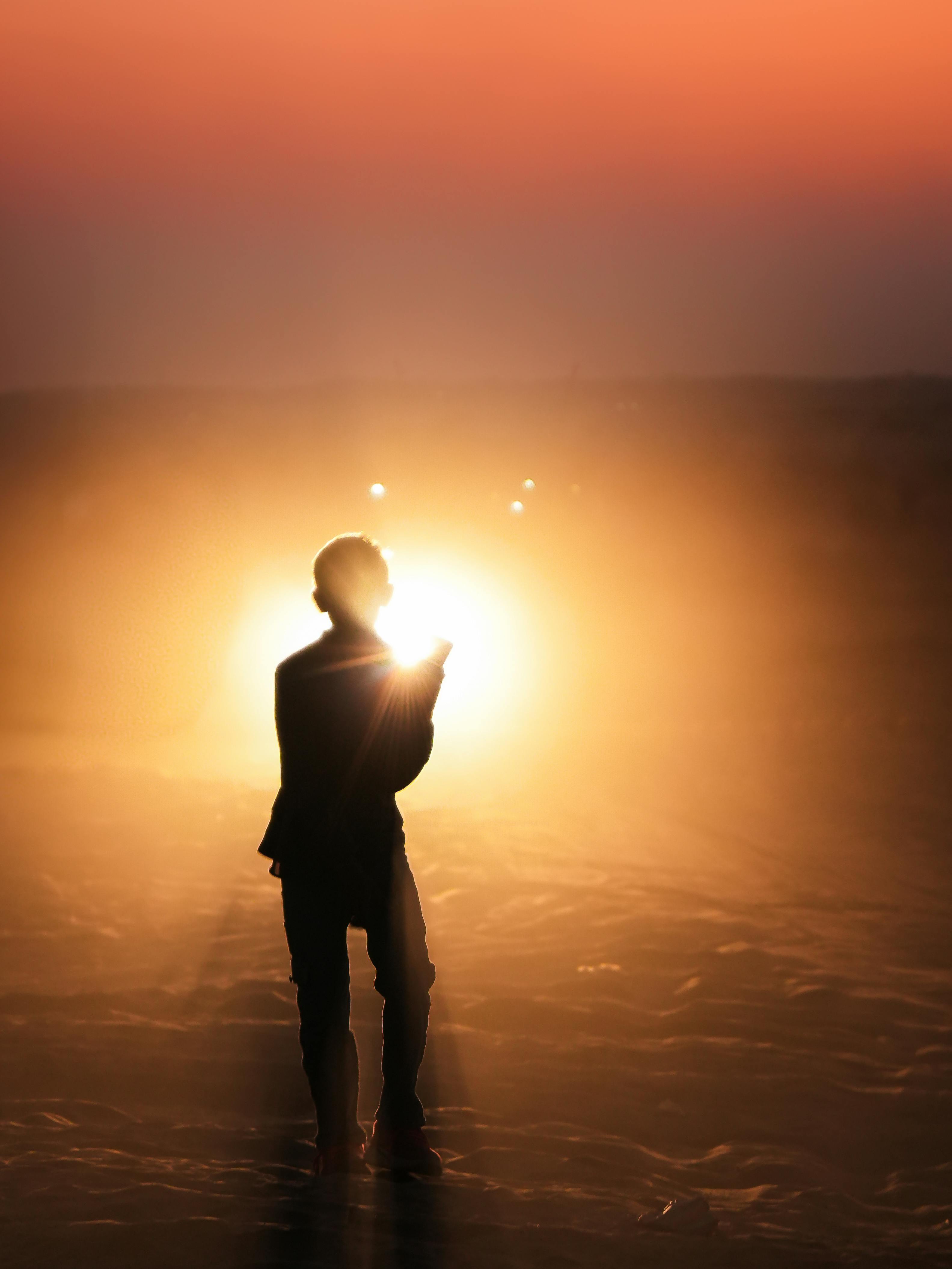 Ücretsiz Canlı turuncu ve altın tonlarının sahneyi sardığı, huzurlu bir gün batımının tadını çıkaran bir kişinin silueti. Stok Fotoğraflar