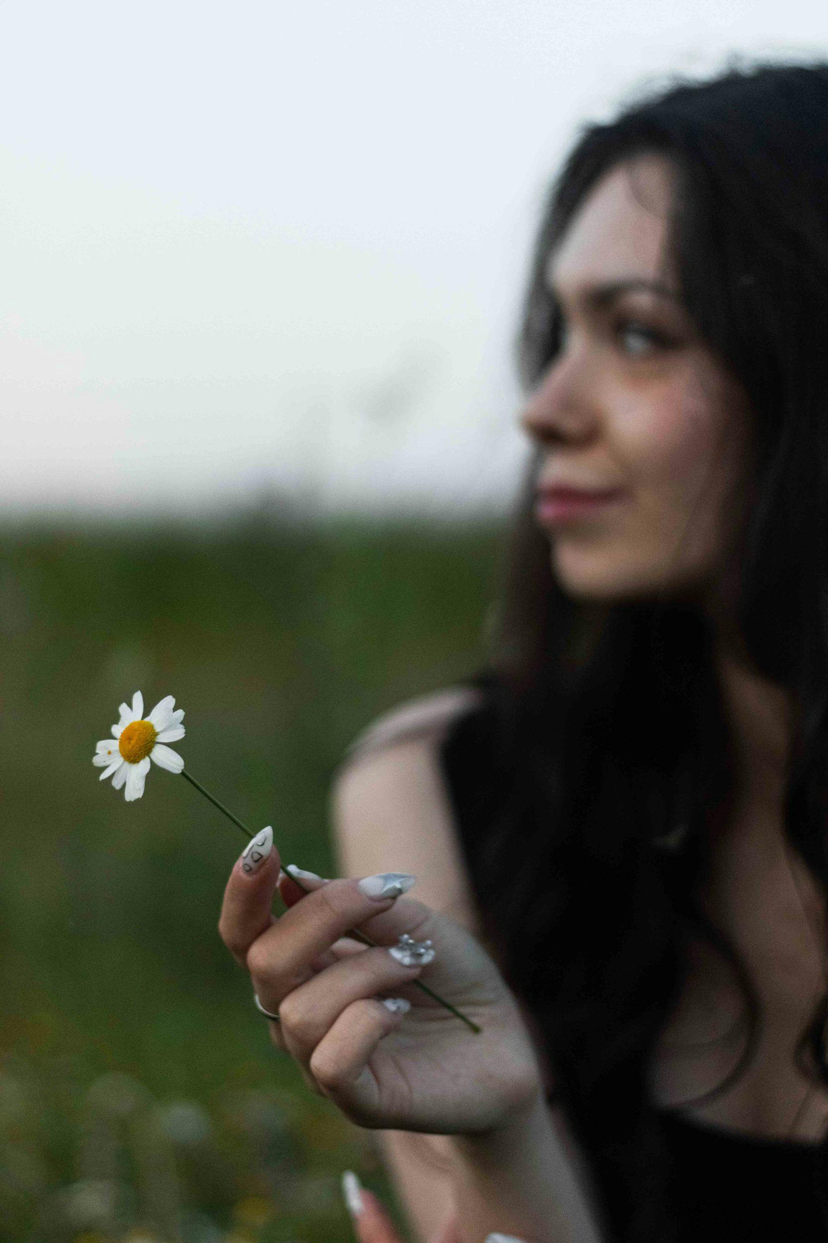 Bezpłatne Zamyślona kobieta trzyma stokrotkę i cieszy się pięknem natury. Zdjęcie z galerii