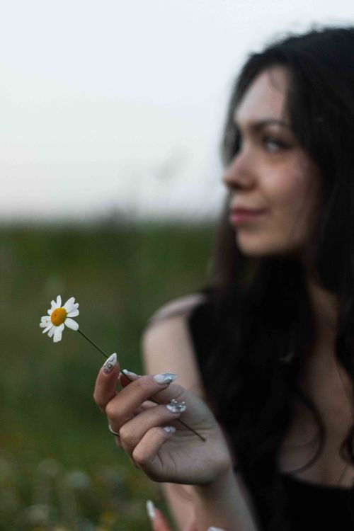 Free Thoughtful woman holding a daisy, enjoying nature's beauty. Stock Photo