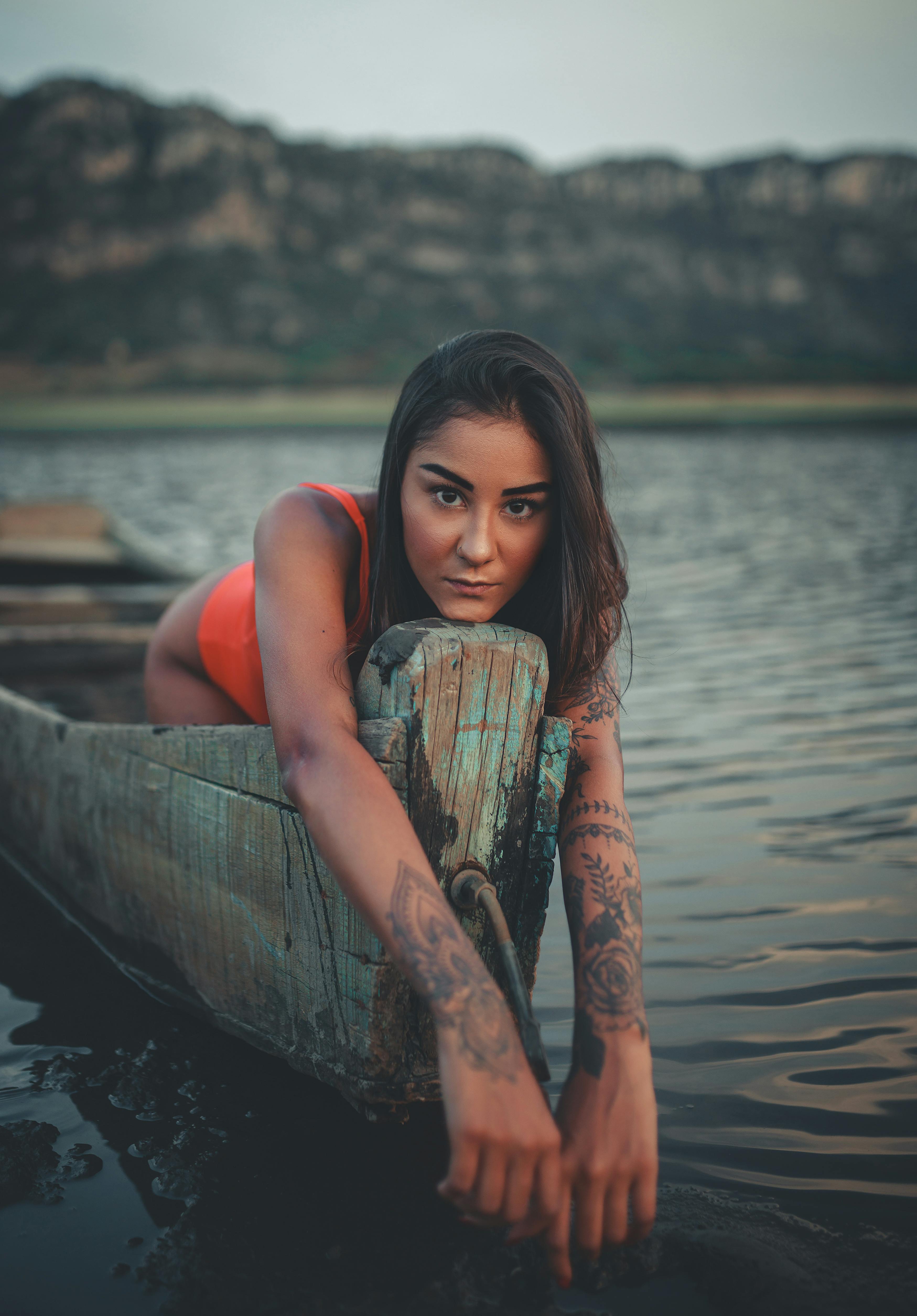 平静的水面上，一艘小船里坐着一名纹身女子，散发着宁静而冒险的氛围
