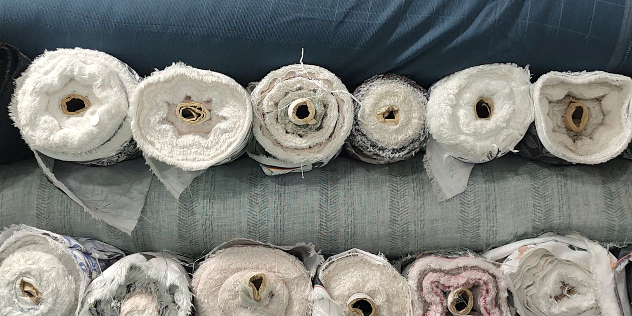 Các cuộn vải polyester và vải pha chồng lên nhau tại cửa hàng dệt may — tiêu chí chọn vải polyester sỉ