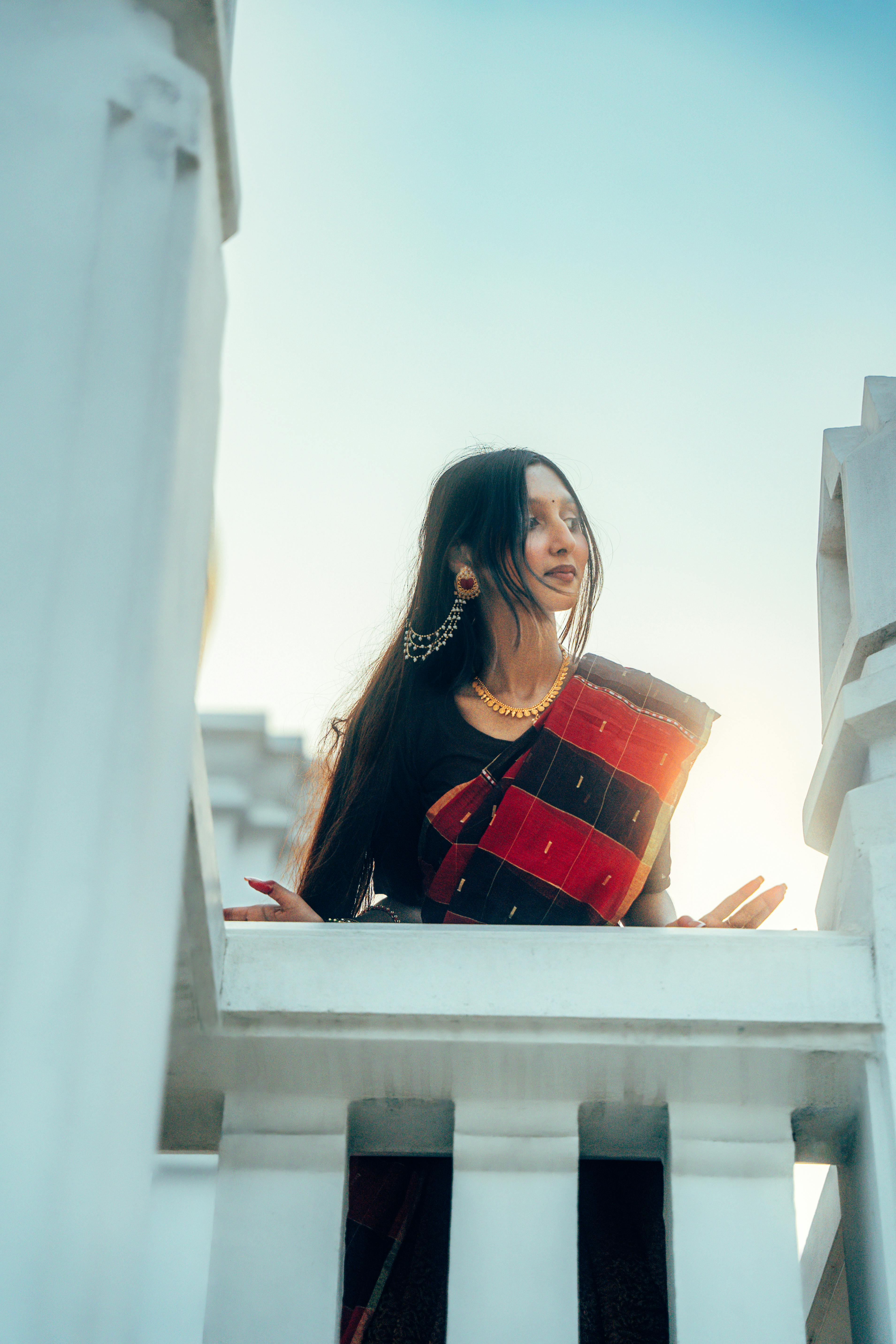 Bezpłatne Młoda kobieta z Azji Południowej ubrana w tradycyjny strój na balkonie, emanująca elegancją i pięknem kulturowym. Zdjęcie z galerii