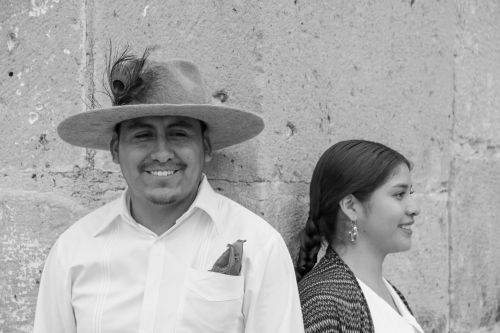 Free A couple in traditional attire smiles against a stone wall. Black and white photo captures cultural heritage. Stock Photo