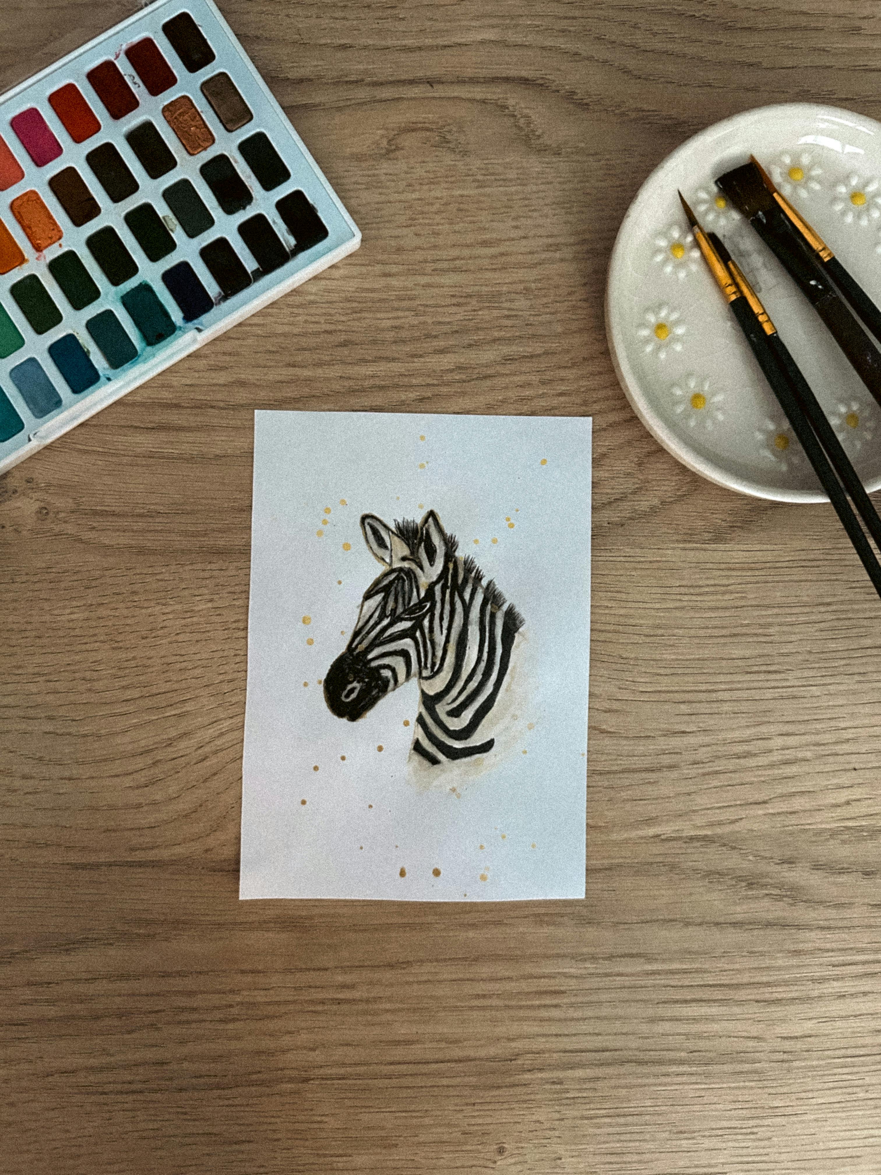 Bezpłatne Artystyczny obraz akwarelowy przedstawiający zebrę otoczoną narzędziami malarskimi na drewnianym stole. Zdjęcie z galerii