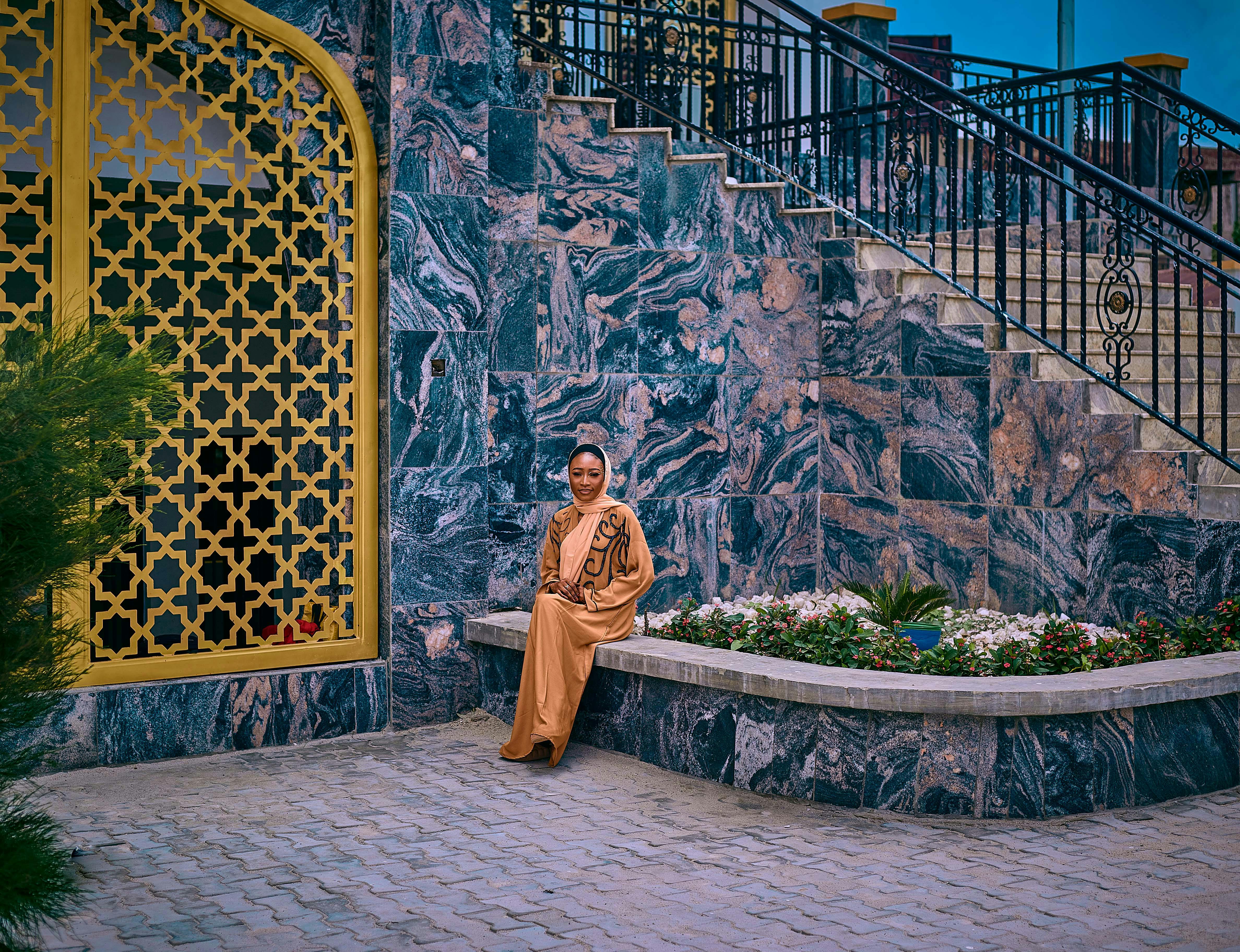 Bezpłatne Kobieta w tradycyjnym stroju siedzi z gracją przy marmurowej ścianie pod błękitnym niebem. Zdjęcie z galerii