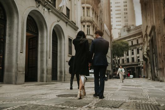 A stylish couple strolls through a historic city street surrounded by iconic architecture.