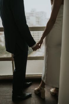 A couple holding hands near a city window in an elegant setting, showcasing love and intimacy.