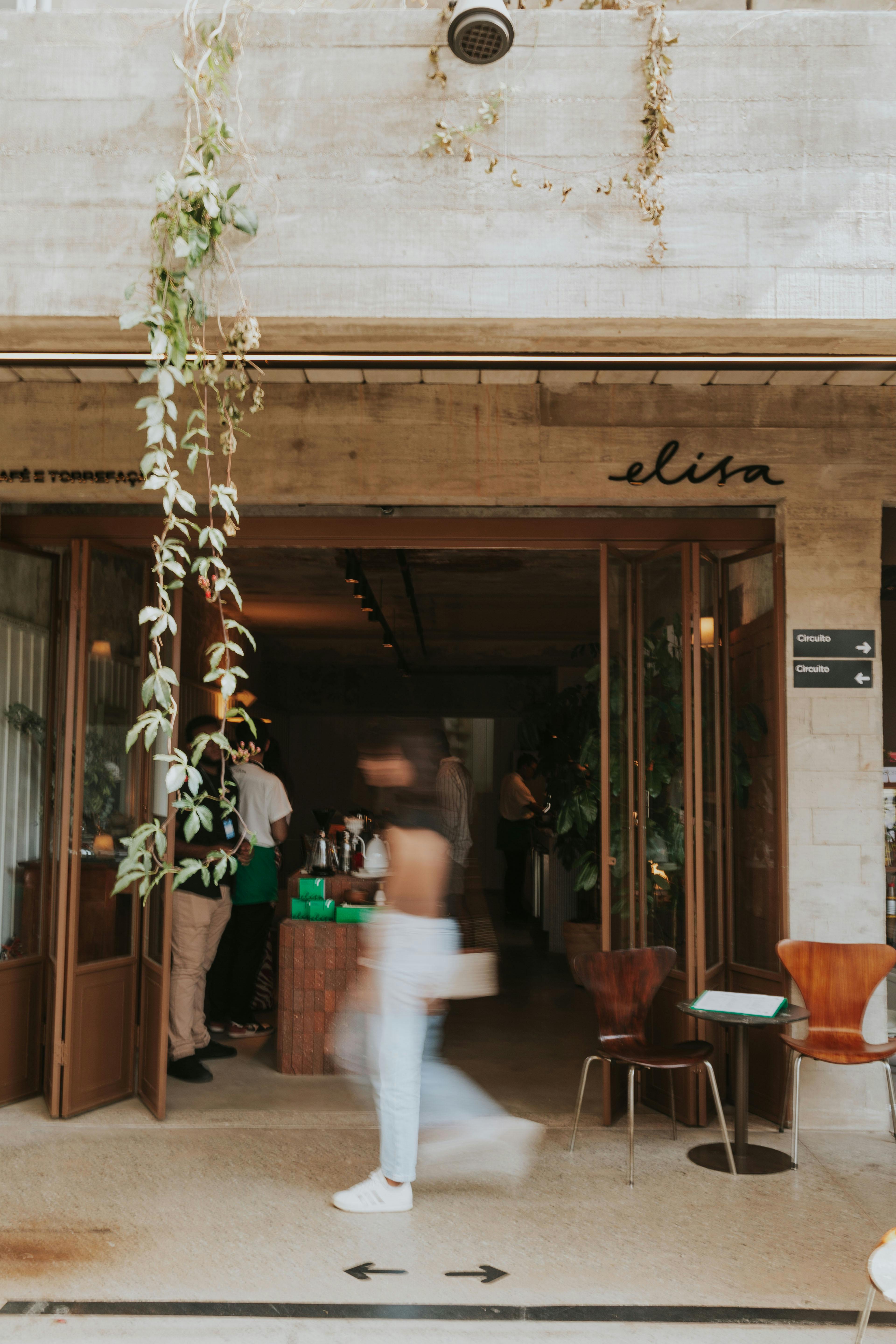 Gratis L'ingresso di un bar elegante, dal design moderno e impreziosito da piante, presenta l'immagine sfocata di una persona che passa. Foto a disposizione