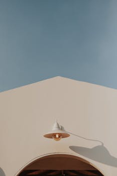 A modern minimalist building with a white facade, outdoor lamp, and clear blue sky.