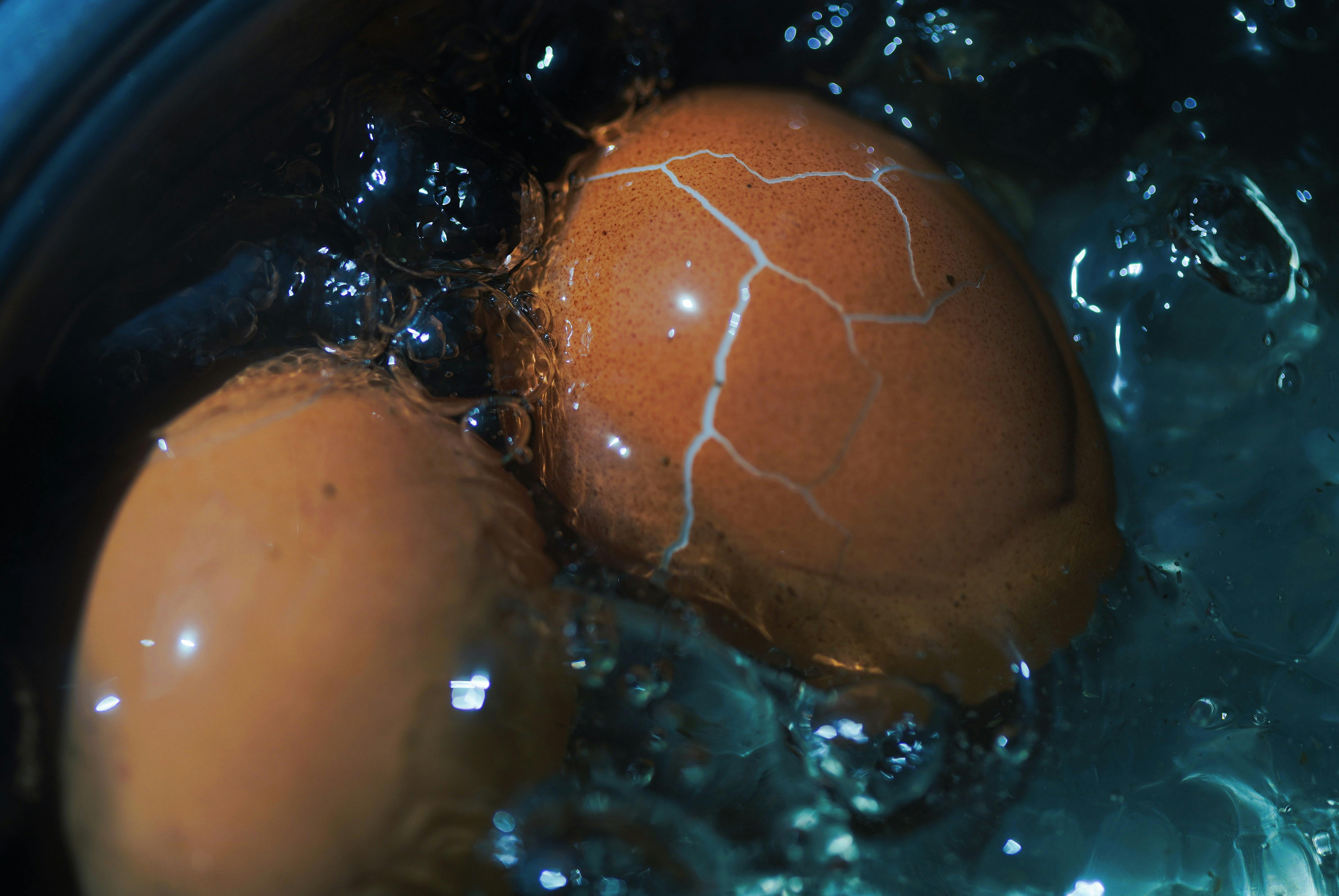 Close-up view of a cracked brown egg boiling in water, showcasing texture and cooking process.