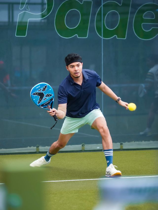 A player in a navy polo steps into a low forehand on a green padel court