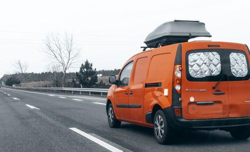 Free Bright orange van traveling on an empty highway with a roof box on a cloudy day. Stock Photo