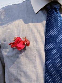 Close-up of a person wearing a grey shirt and blue tie adorned with red flowers