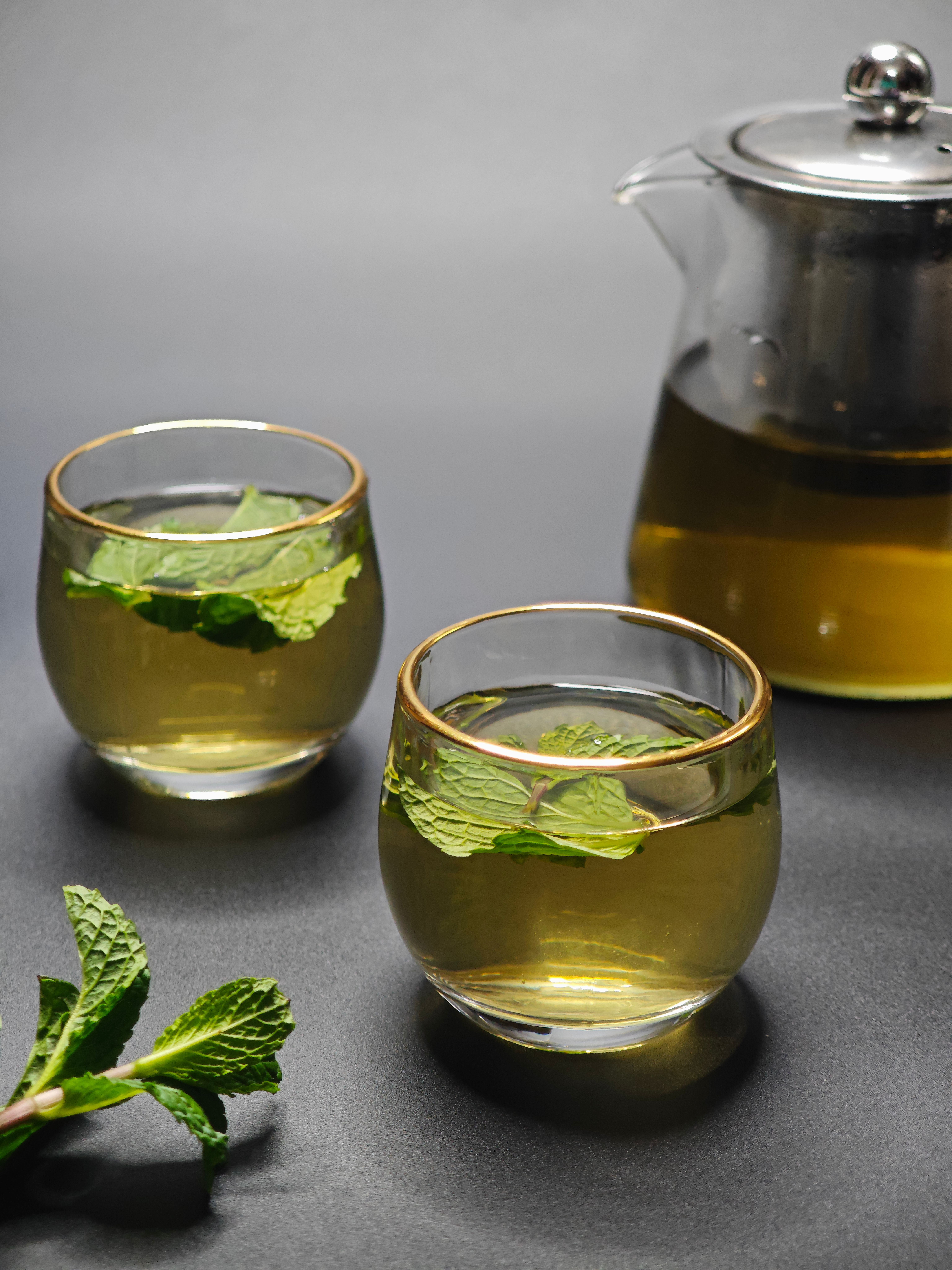 Close-up of mint tea in glass cups with a glass teapot and mint leaves.