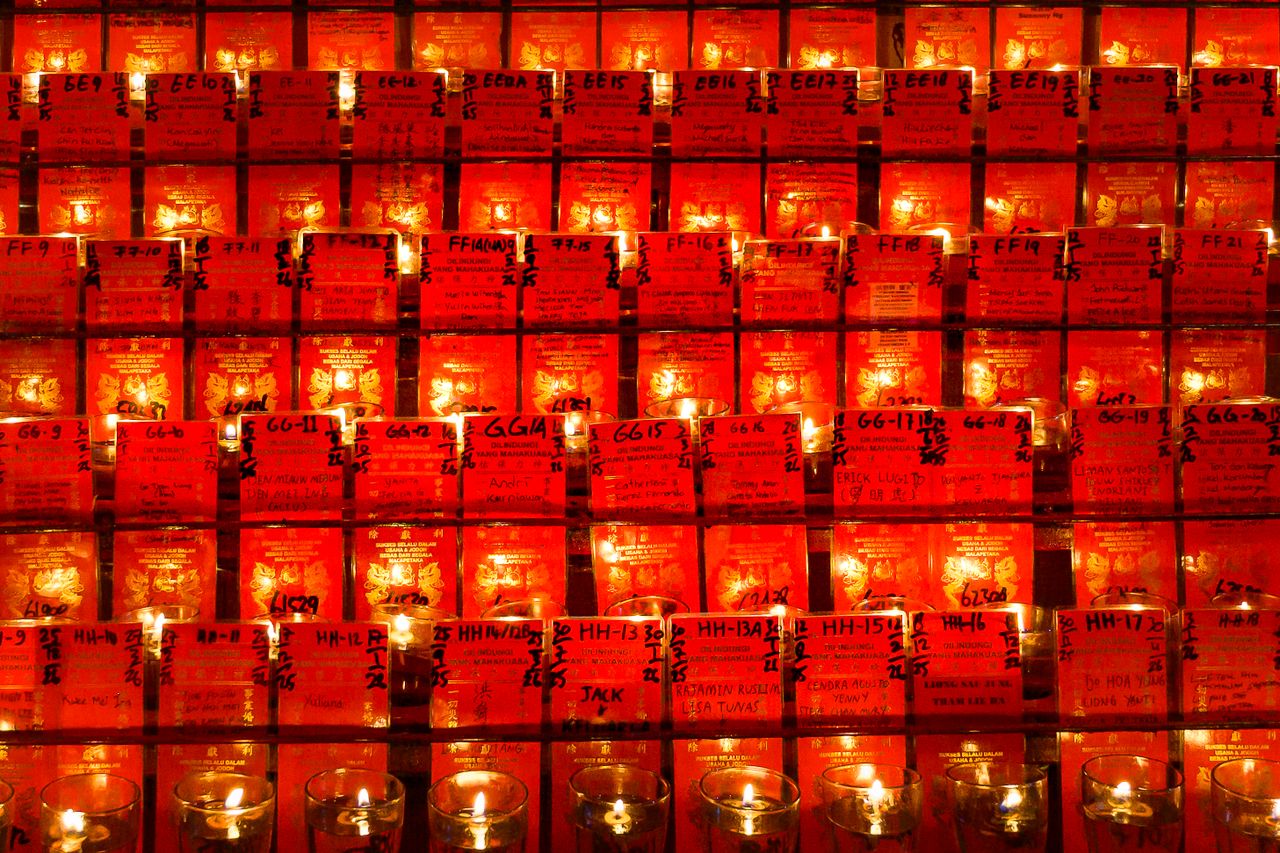 a collection of votive candles set against a wall of red cards creatin