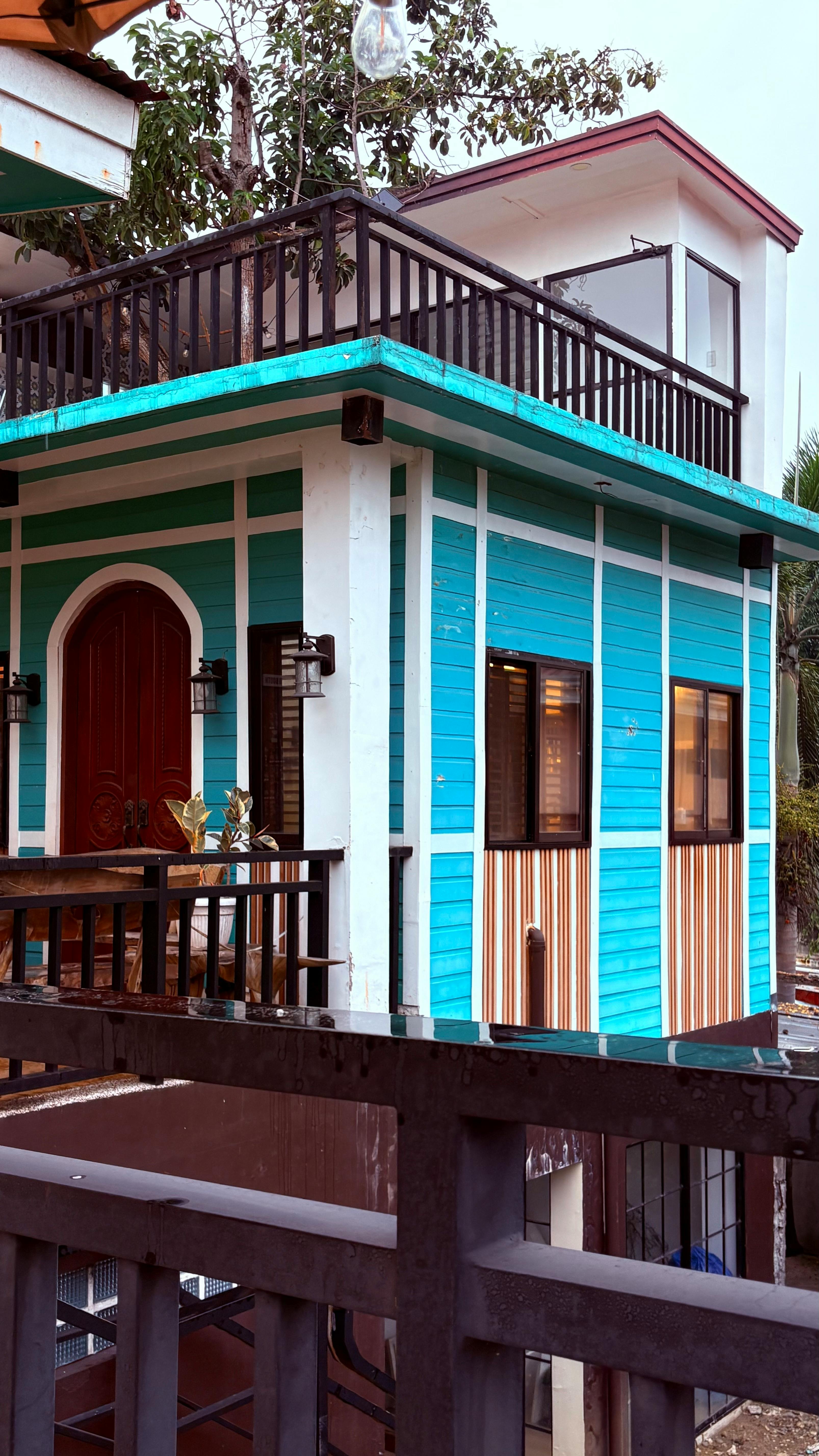 Gratis Rumah berwarna biru kehijauan dan cokelat yang cerah, dilengkapi balkon dan elemen desain modern. Foto Stok