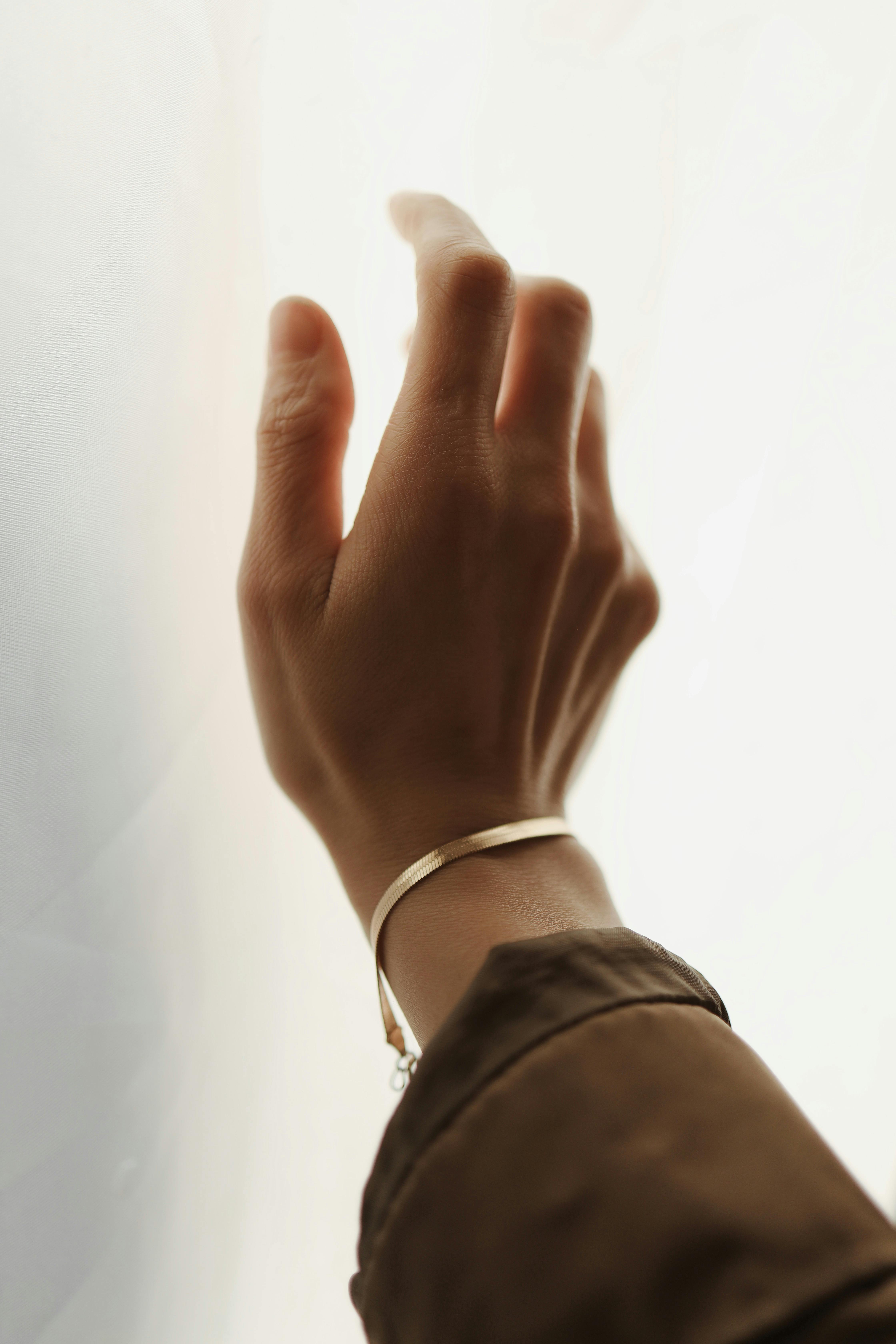 Kostenlos Eine Nahaufnahme einer Hand mit Armband, die sich nach sanftem Licht ausstreckt und Eleganz und Offenheit vermittelt. Stock-Foto