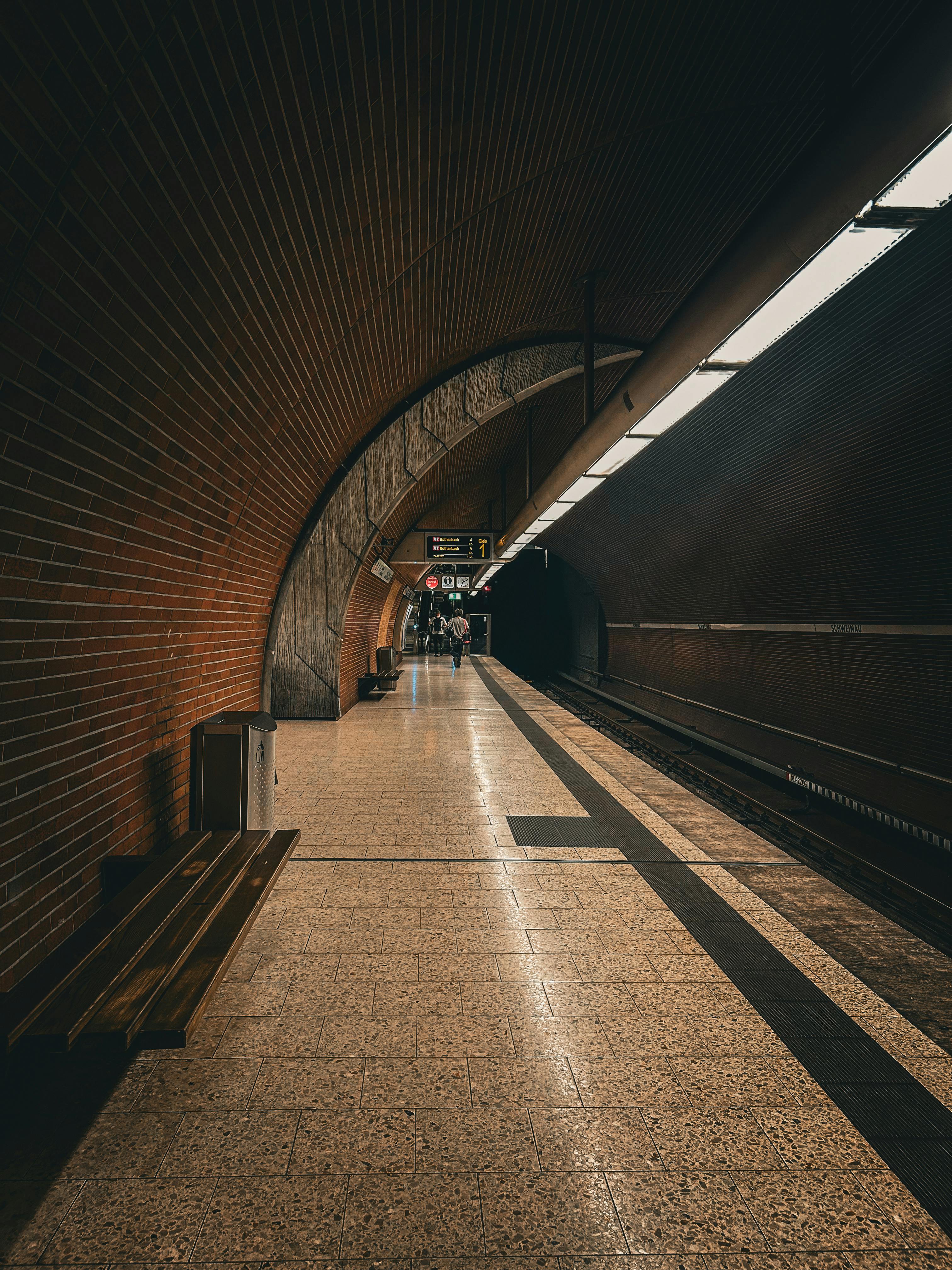 A dimly lit subway station platform with a curved brick wall and people in the distance.