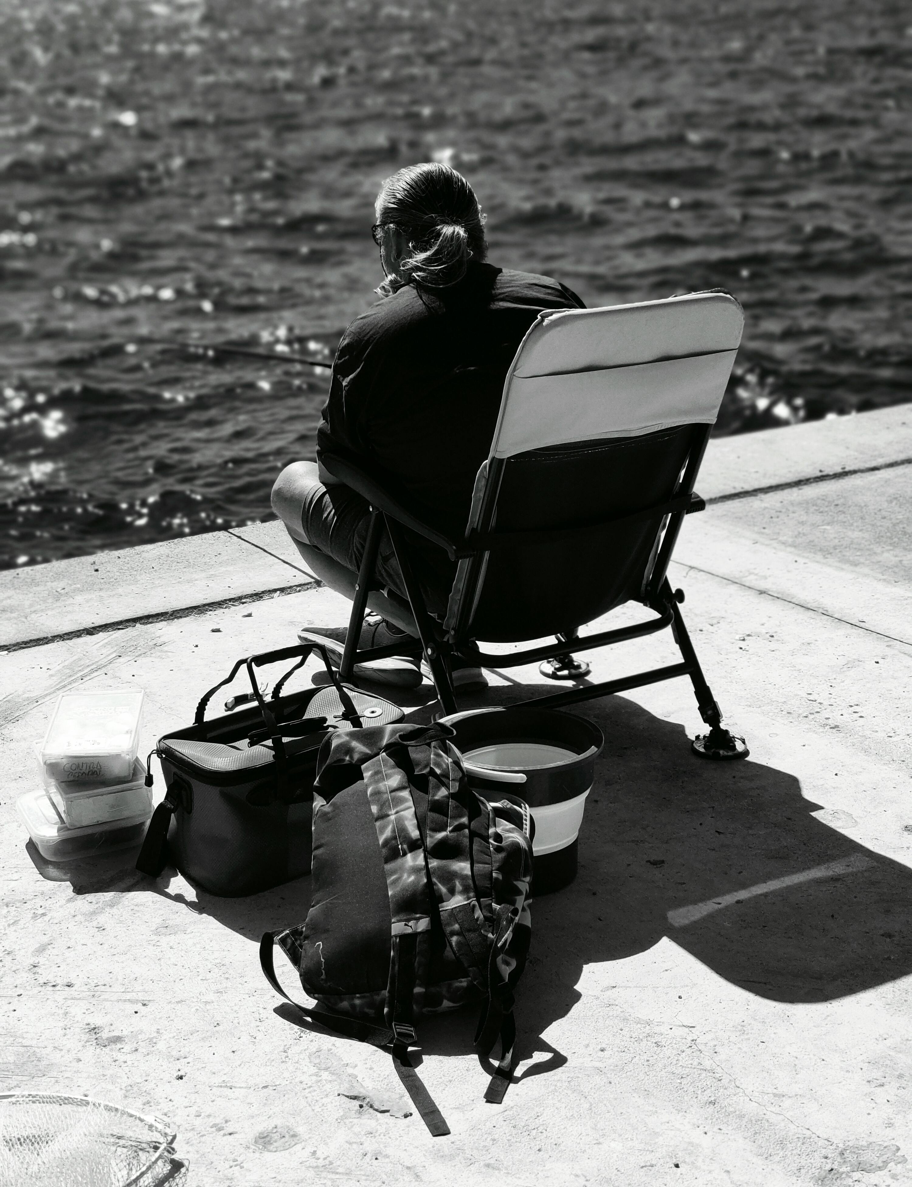 Bezpłatne Osoba siedząca nad wodą z krzesłem i torbami, ciesząca się chwilą spokoju. Zdjęcie z galerii