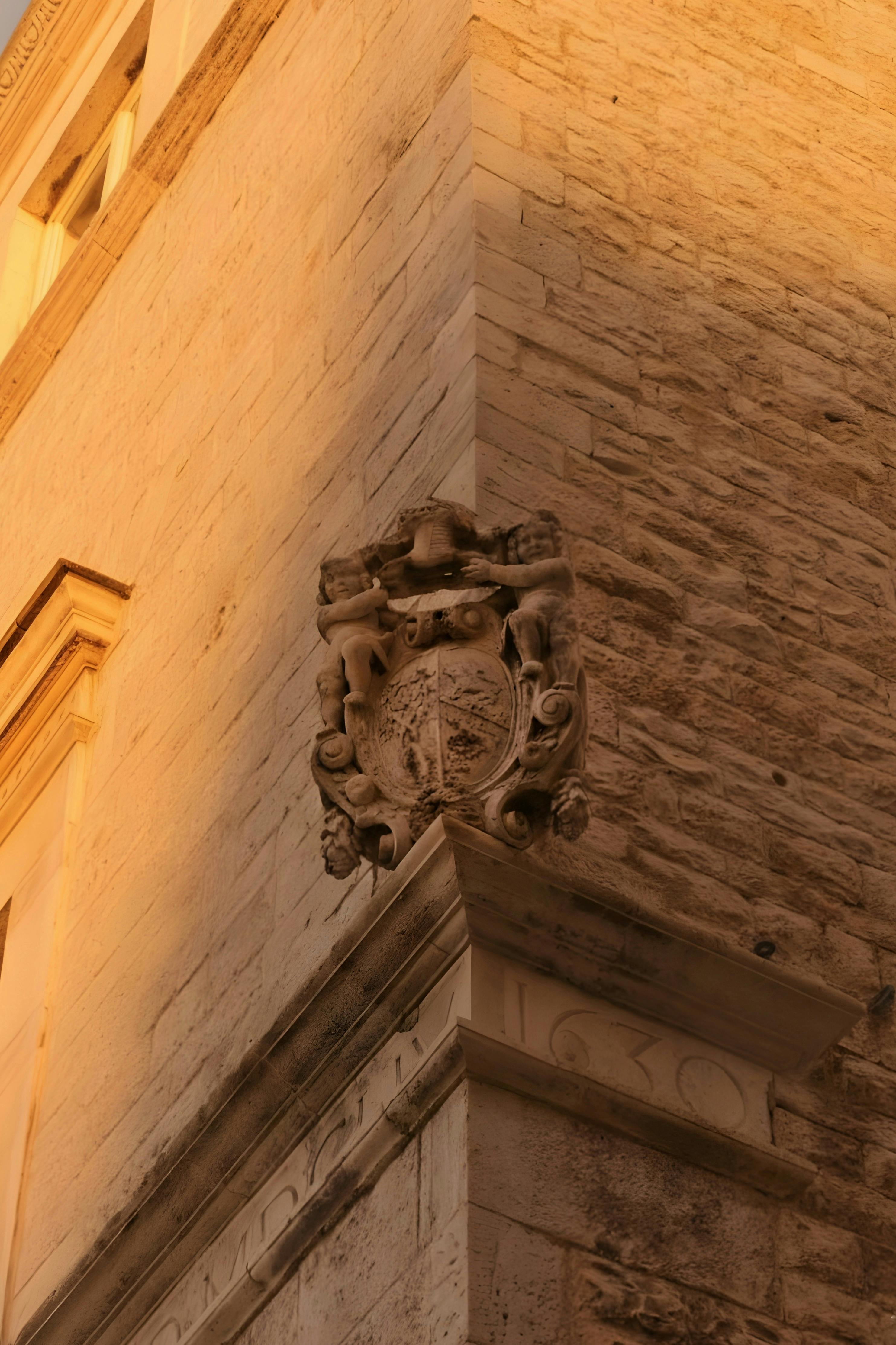 Bezpłatne Zbliżenie na oświetlone słońcem kamienne zdobienia na narożniku zabytkowego budynku. Zdjęcie z galerii