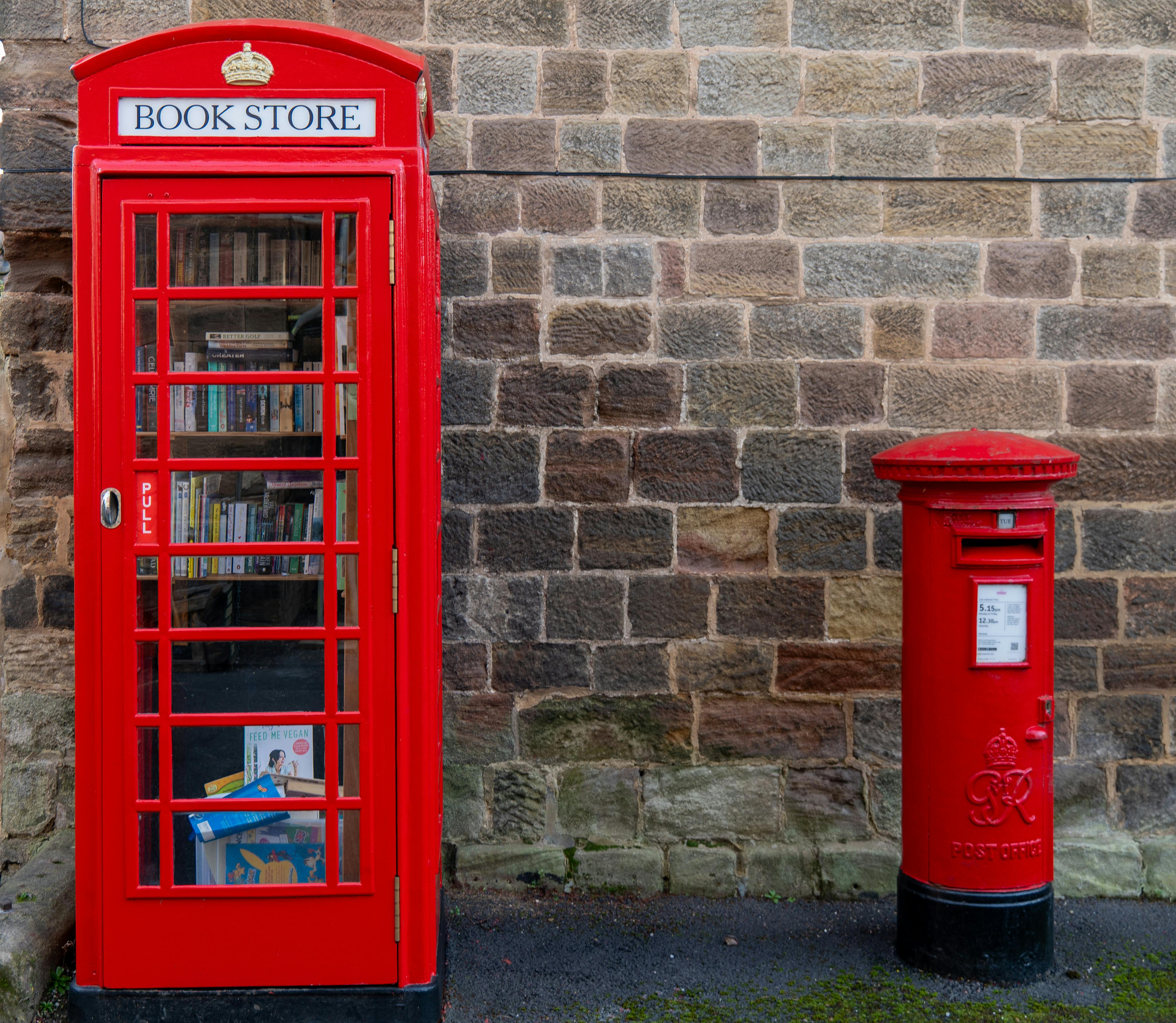 Charming red telephone box turned local bookstore next to a historic postbox in Ripley, UK.