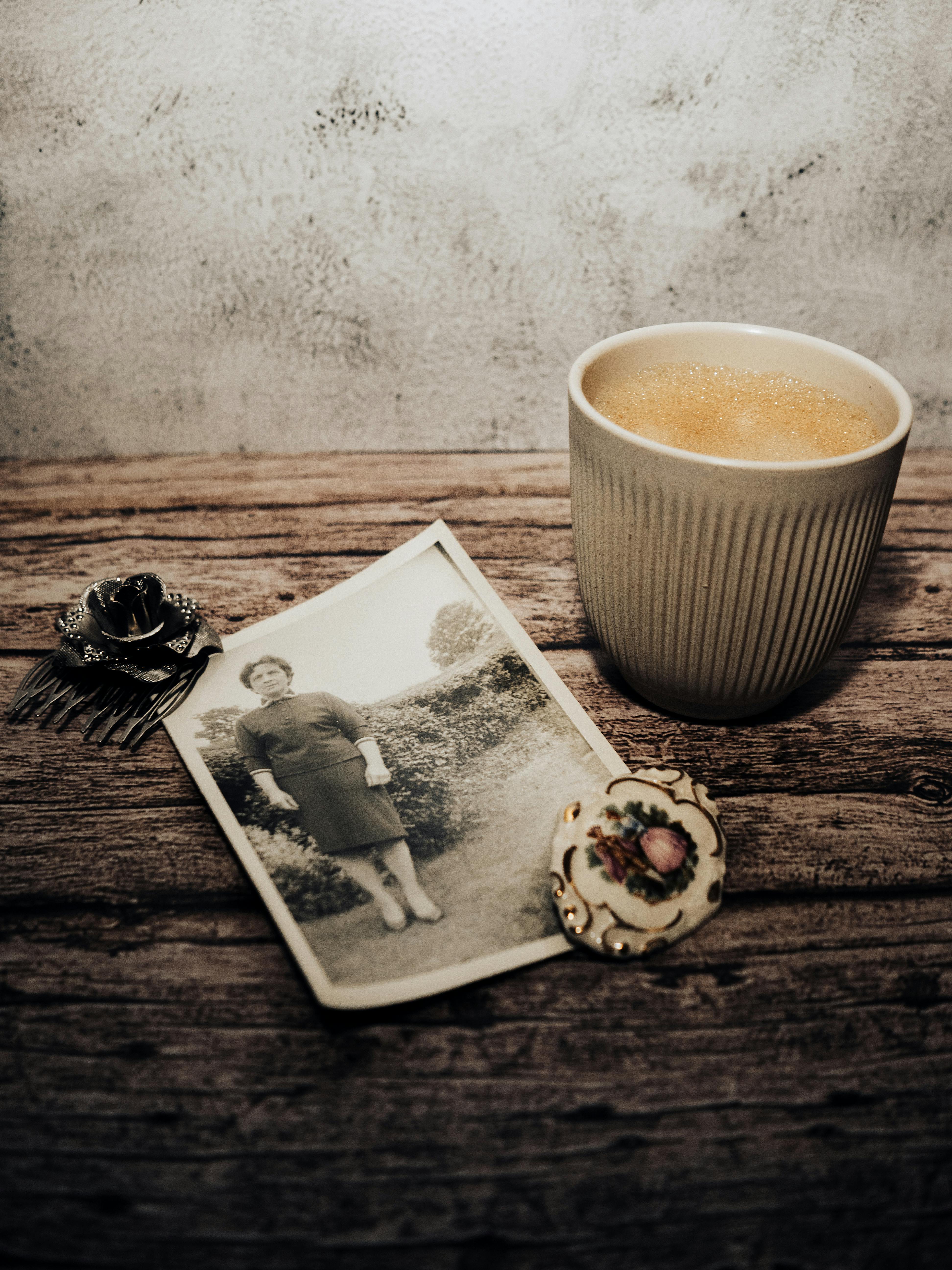 Bezpłatne Nostalgiczna martwa natura przedstawiająca stare zdjęcie, filiżankę do kawy, spinkę do włosów i ozdobny talerz na rustykalnym drewnie. Zdjęcie z galerii