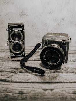 An artistic shot of two vintage twin-lens reflex cameras on a rustic wooden background.