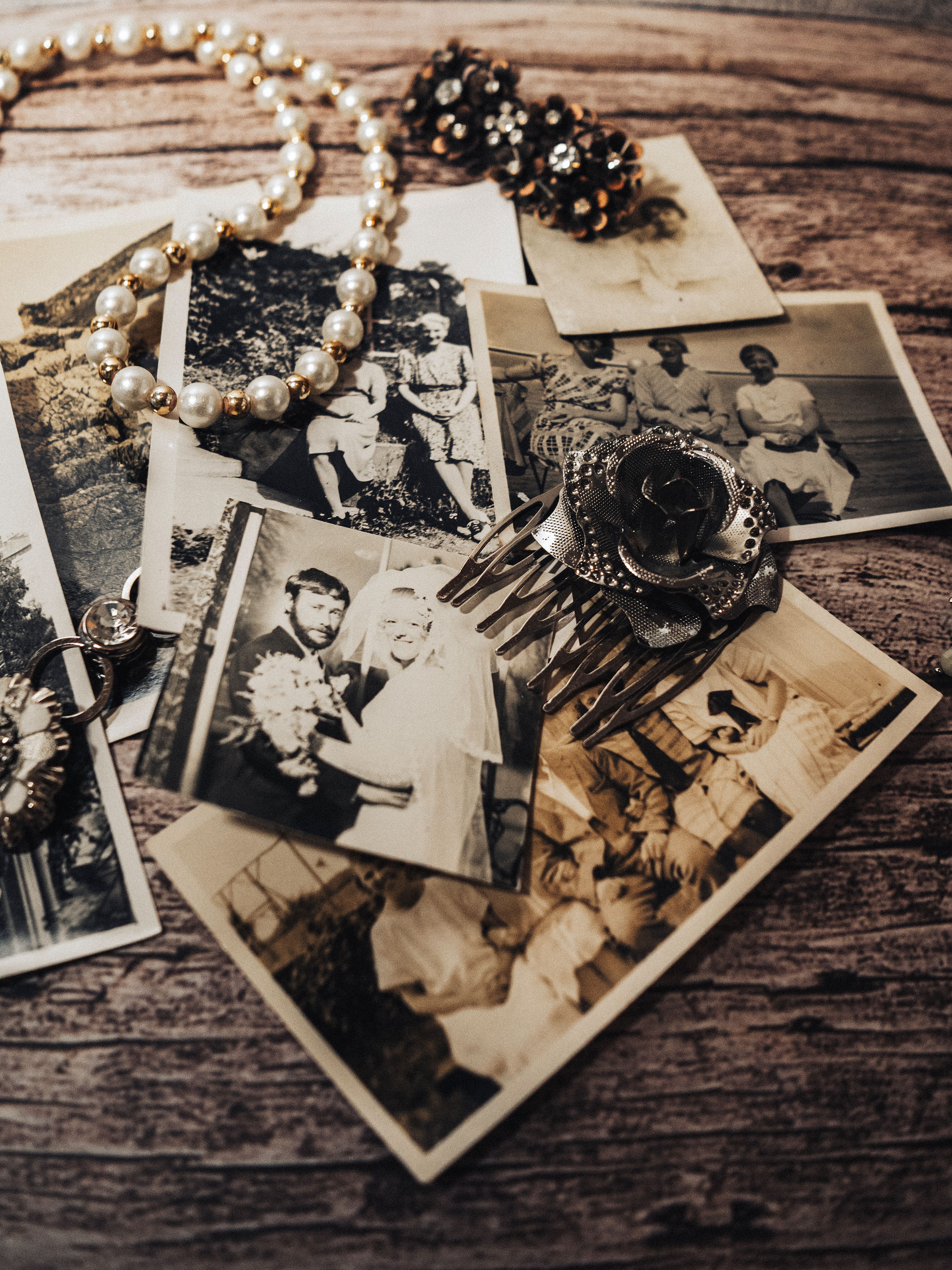 A collection of vintage black and white photos with pearl necklace and antique brooch displayed on a rustic wooden table.