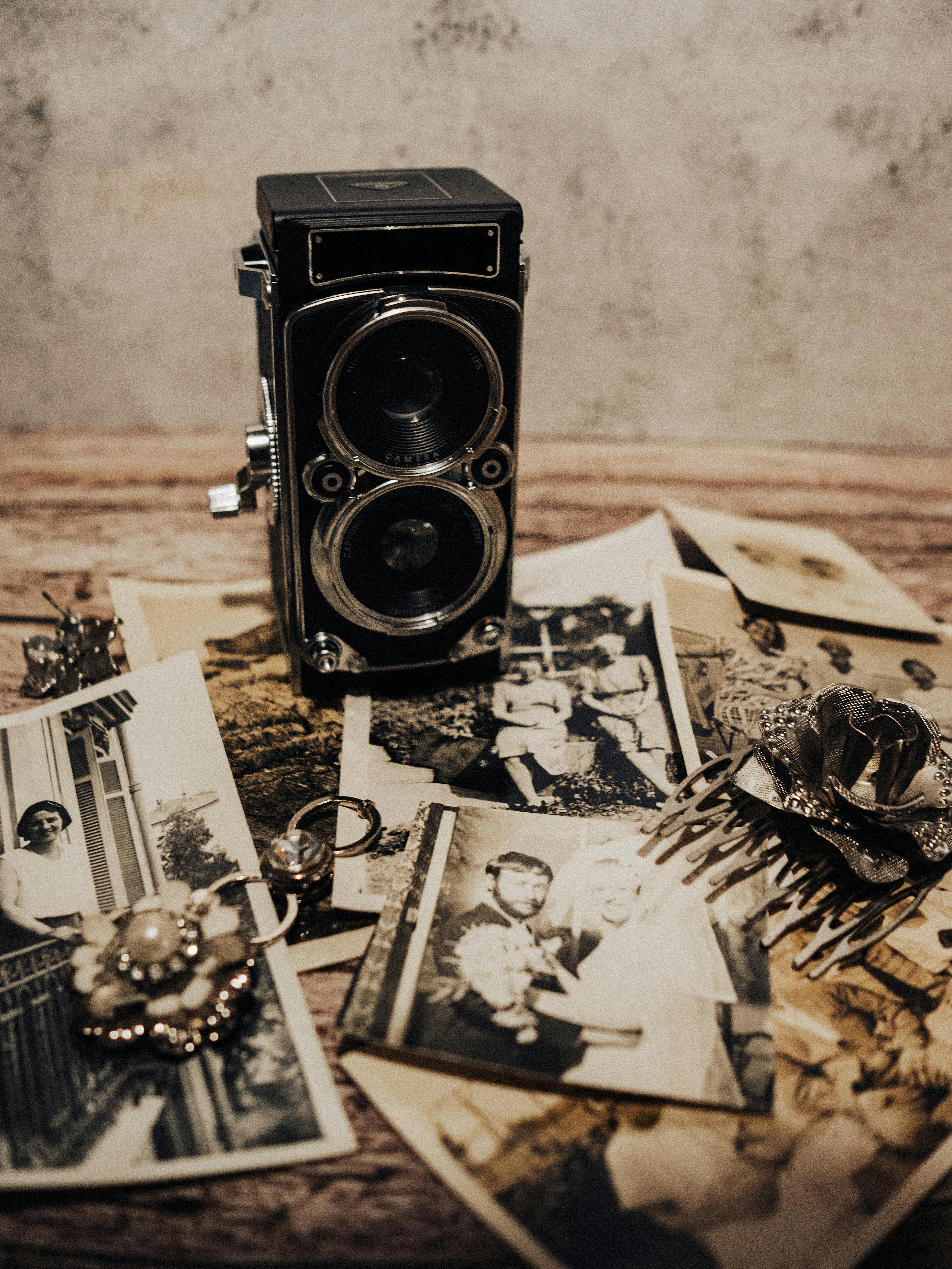 Ücretsiz Ahşap bir yüzey üzerinde, siyah beyaz fotoğraflar ve antika takılarla çevrili retro bir fotoğraf makinesi. Stok Fotoğraflar