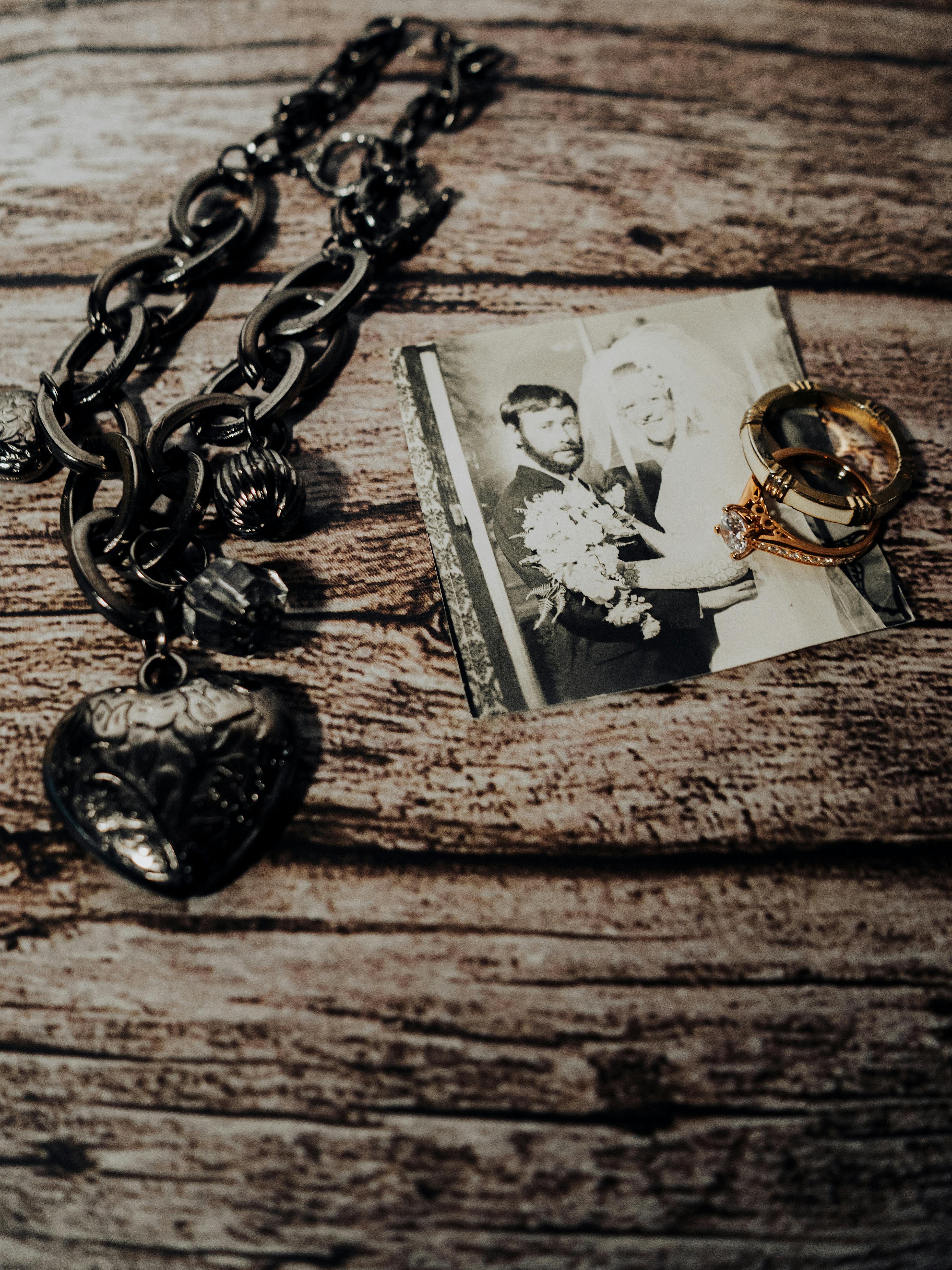 Bezpłatne Nostalgiczna ekspozycja zdjęcia ślubnego, pierścionków i naszyjnika na rustykalnym drewnie. Zdjęcie z galerii