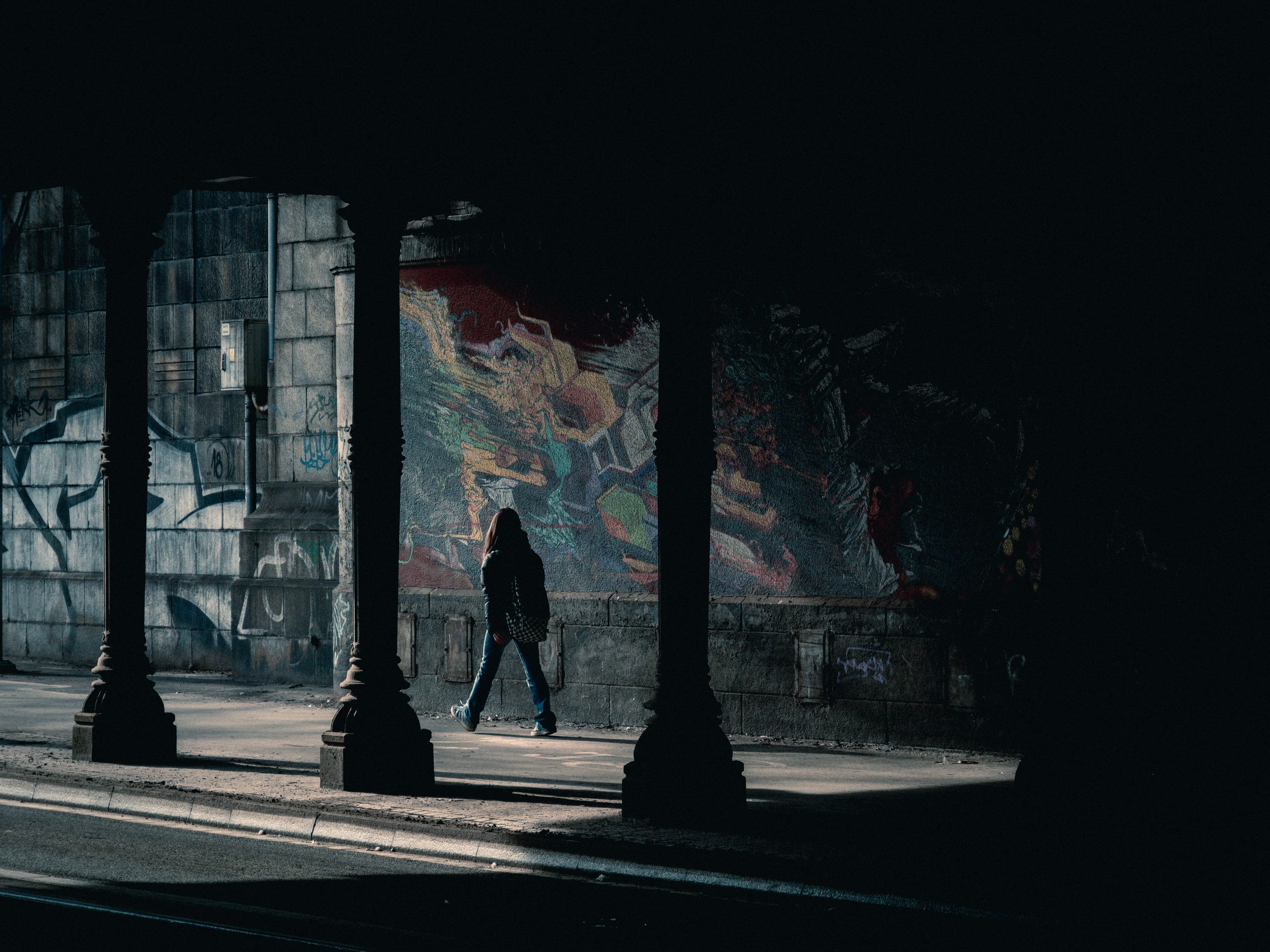 gratis Een persoon loopt door een schaduwrijke stedelijke tunnel met kleurrijke graffitimuren. Stockfoto