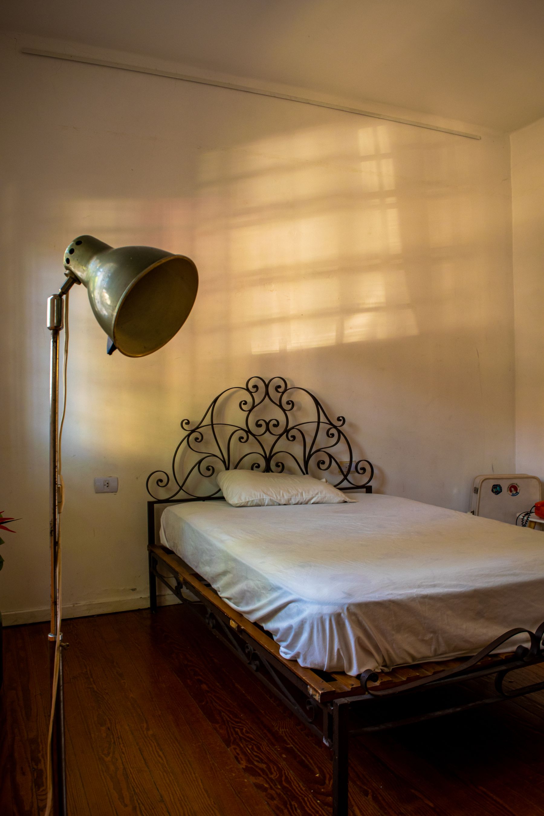 Black scrollwork metal bed with plain white bedding and an adjustable floor lamp