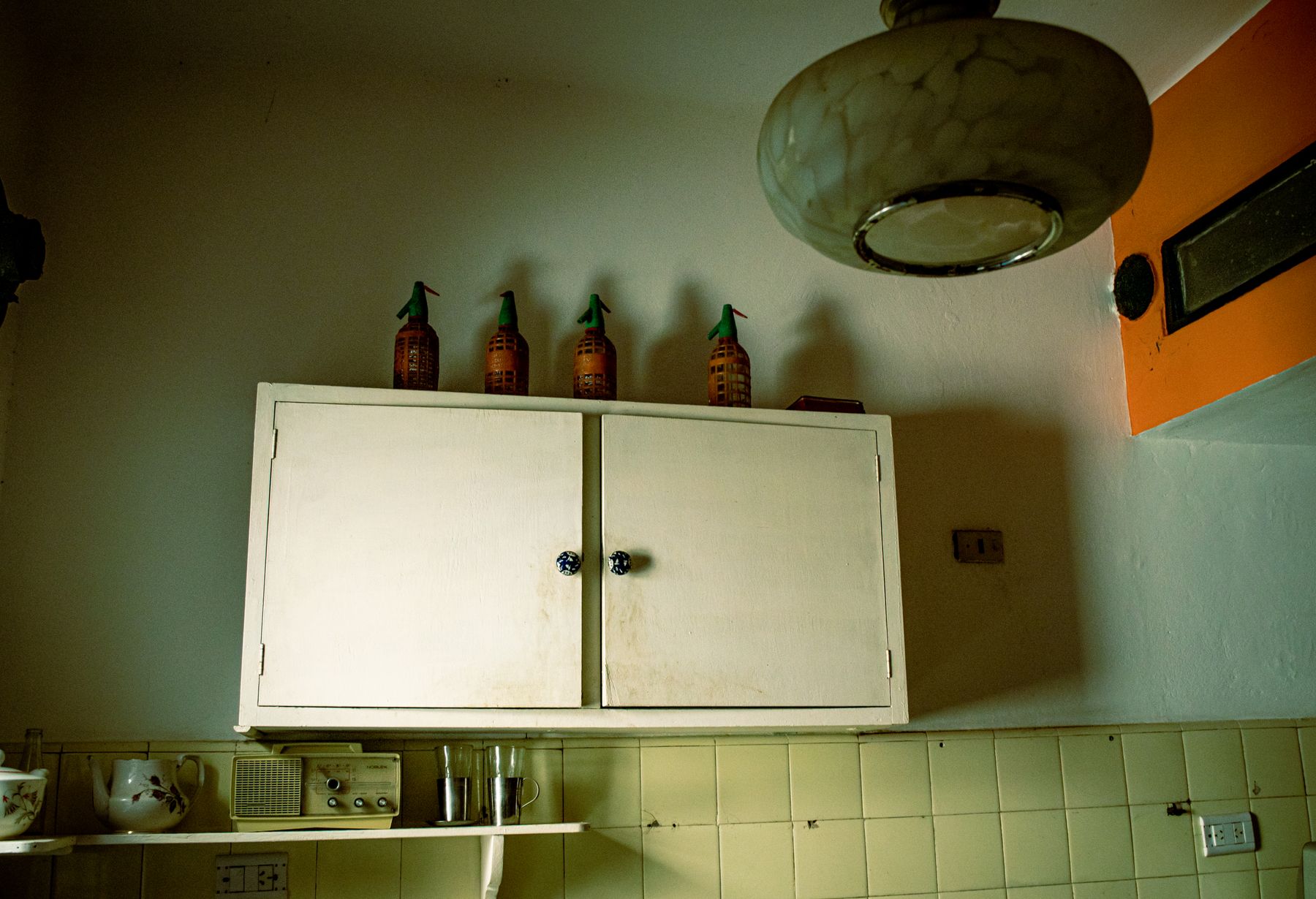 Cream wall cupboard above pale yellow tiles with an old radio and rounded pendant