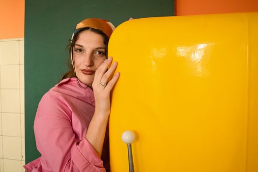 Woman in a pink blouse embraces a vibrant yellow retro fridge indoors.