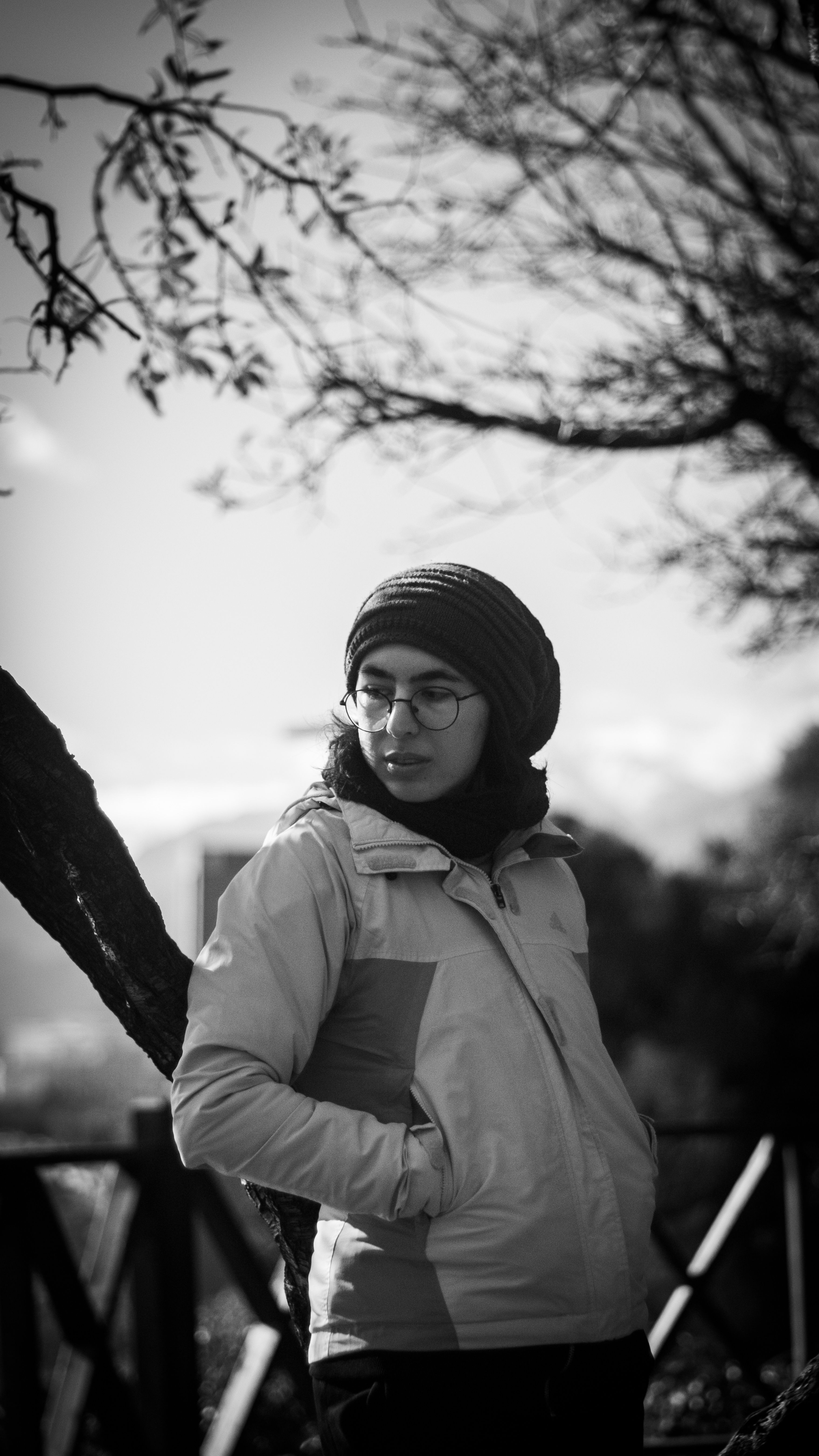Moody black and white portrait of a woman wearing a jacket and beanie outdoors.