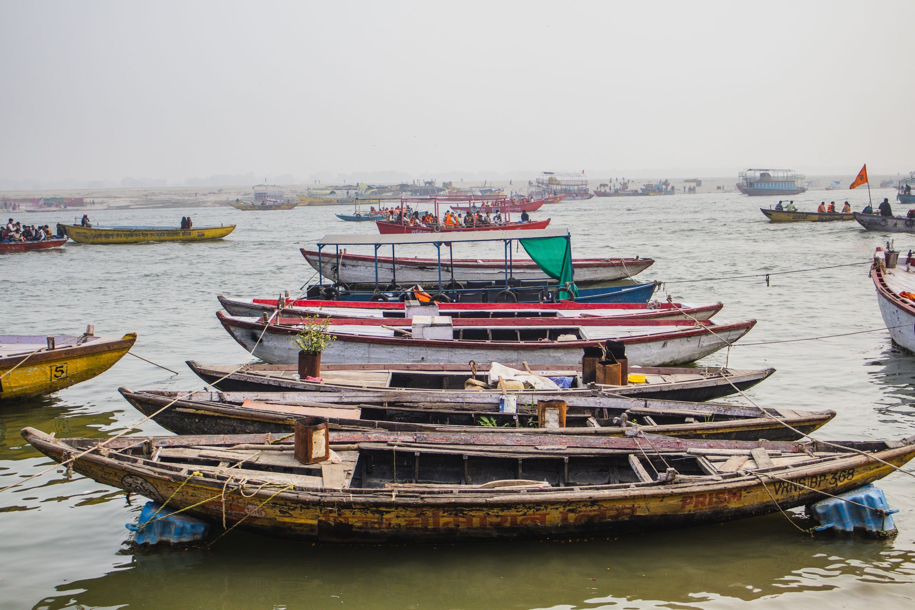 Vibrant boats anchored on a calm river with passengers in the distance, creating a serene scene.